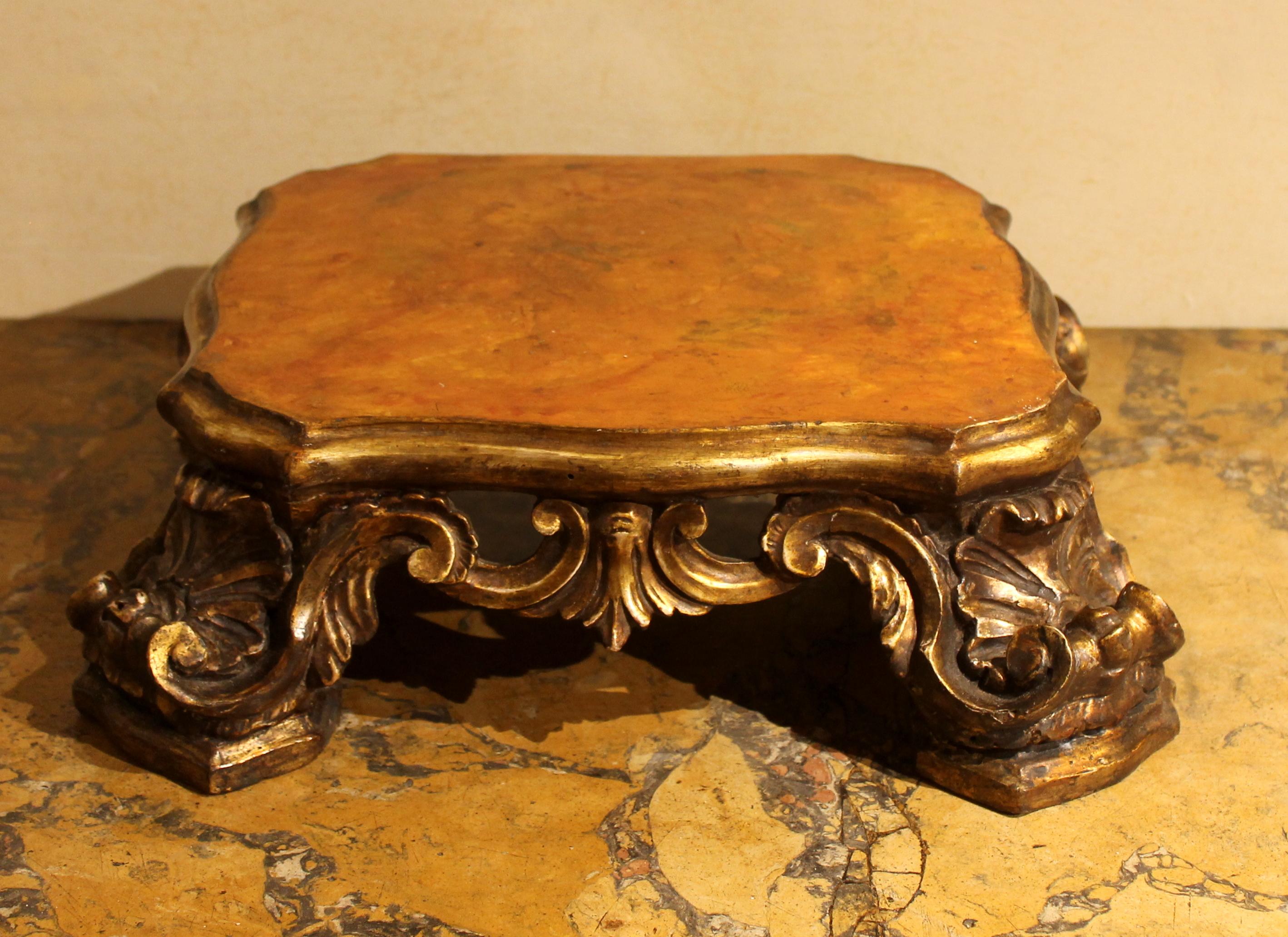 This extremely beautiful entirely hand carved, gilded and lacquered wooden base belongs to the Roman Baroque period. 
This antique pedestal from the 1600s has a beautiful shape, the lacquered faux marble top in orange-yellow to ocher tones rests on