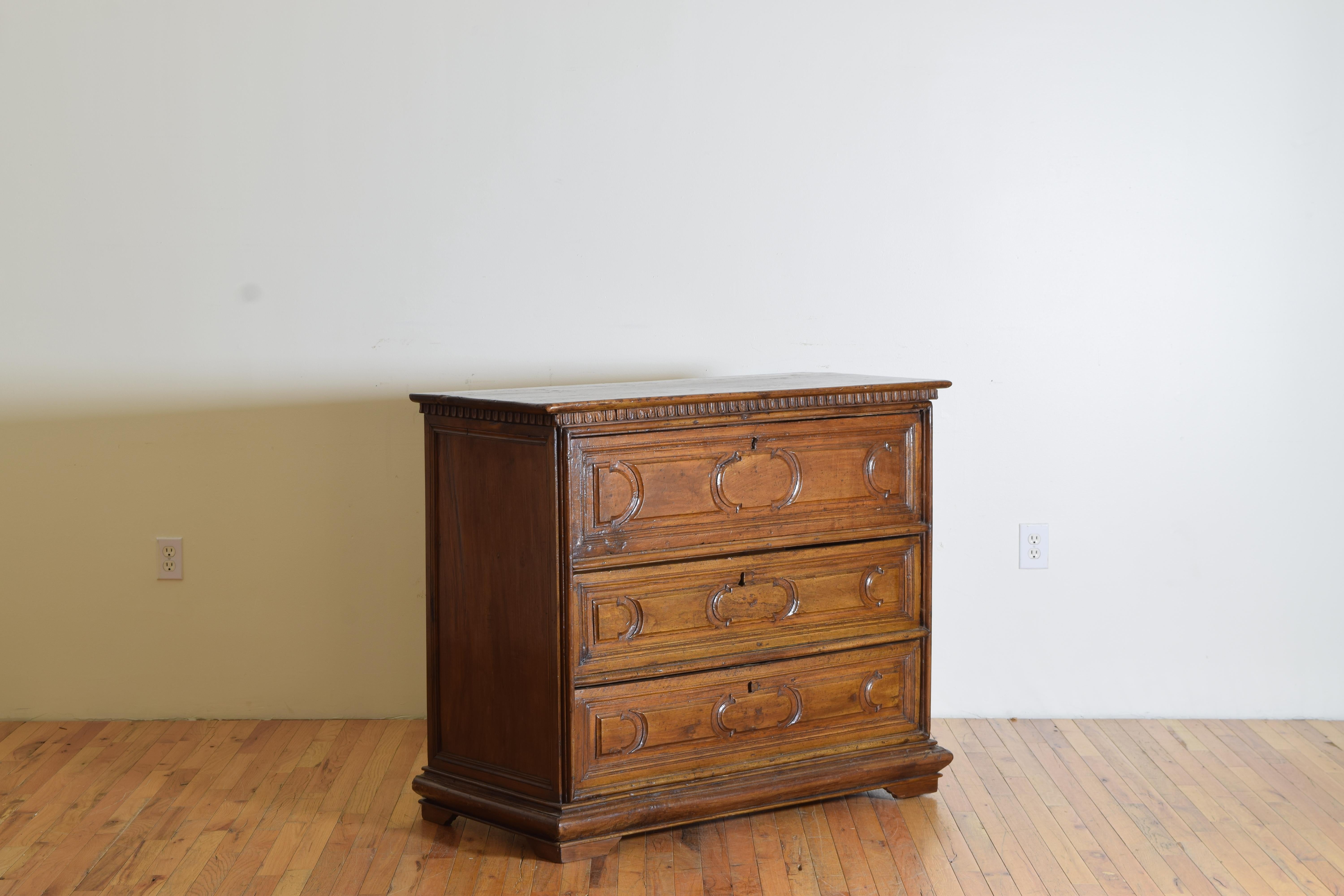 A rectangular top with dentile molding over three drawers having pronounced carved panels on the drawer fronts resting on bracket feet.