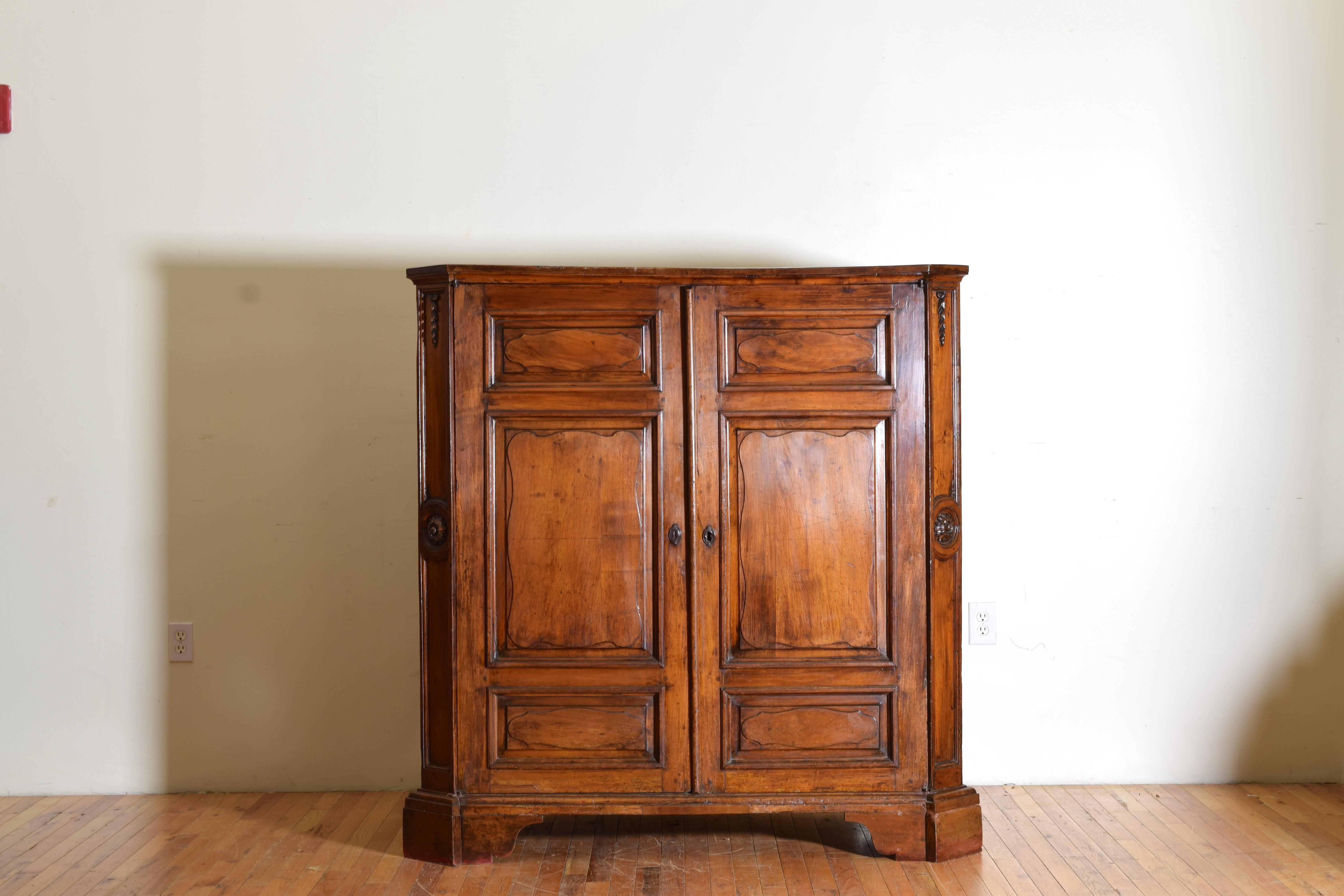 Having a rectangular top with canted corners above a conforming case with carved rosettes at corners and paneled doors and sides, the interior with shelving and a bottom drawer, rasied on a plinth-form base.
