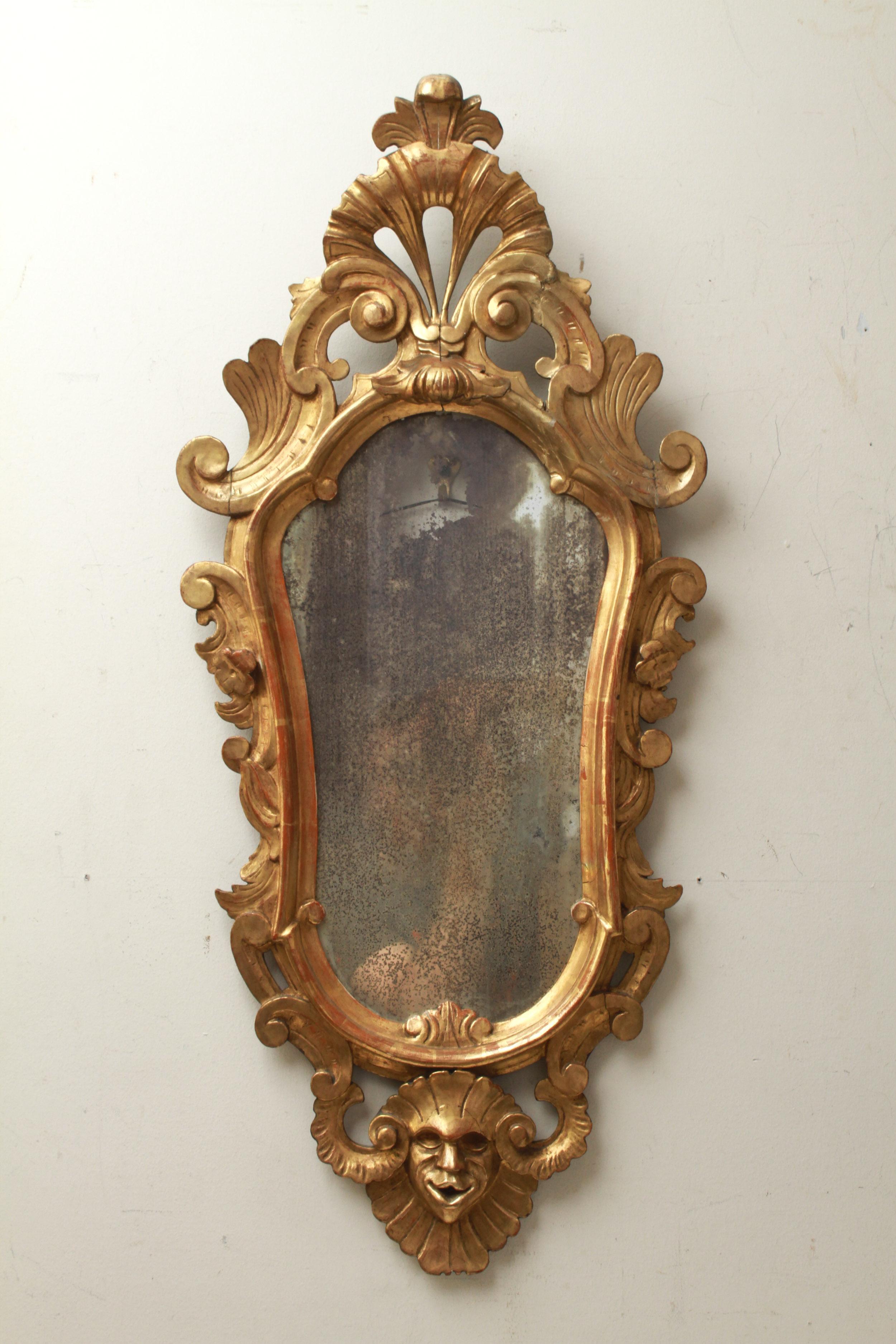 Italian Baroque Revival pair of giltwood mirrors, made in the 19th century. Each mirror has a centered shell cartouche atop and is flanked by C-scrolls ending to a relief-carved mask at the bottom. One with original mirror glass. In great antique