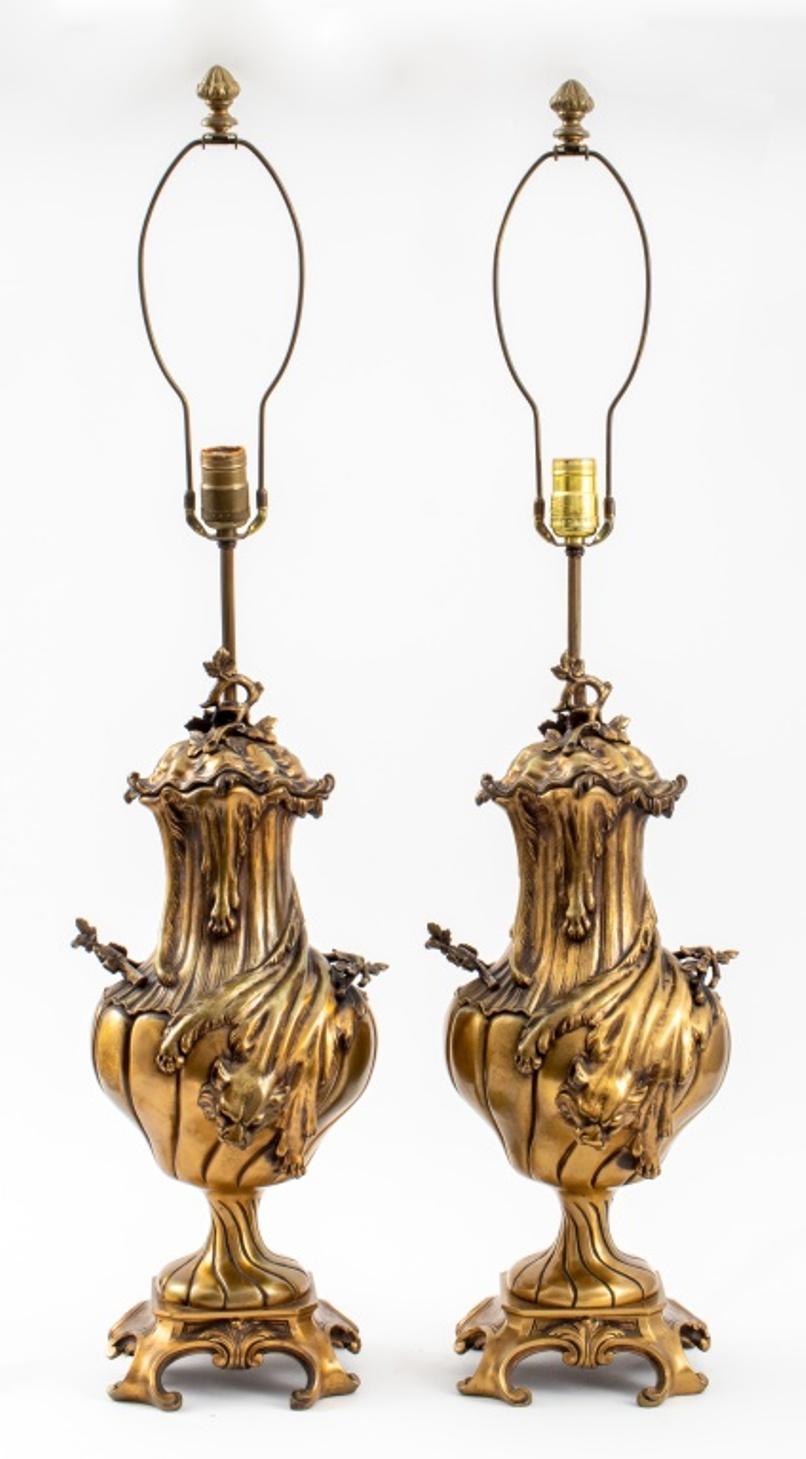 Italian Baroque revival style bronze lamps, a pair, with leafing vine fiinal above a clamshell form lid, above an urn shaped body cast with draped lioness pelts nd leafing grapevine handles, the diagonally turned body and socle on scroll form footed