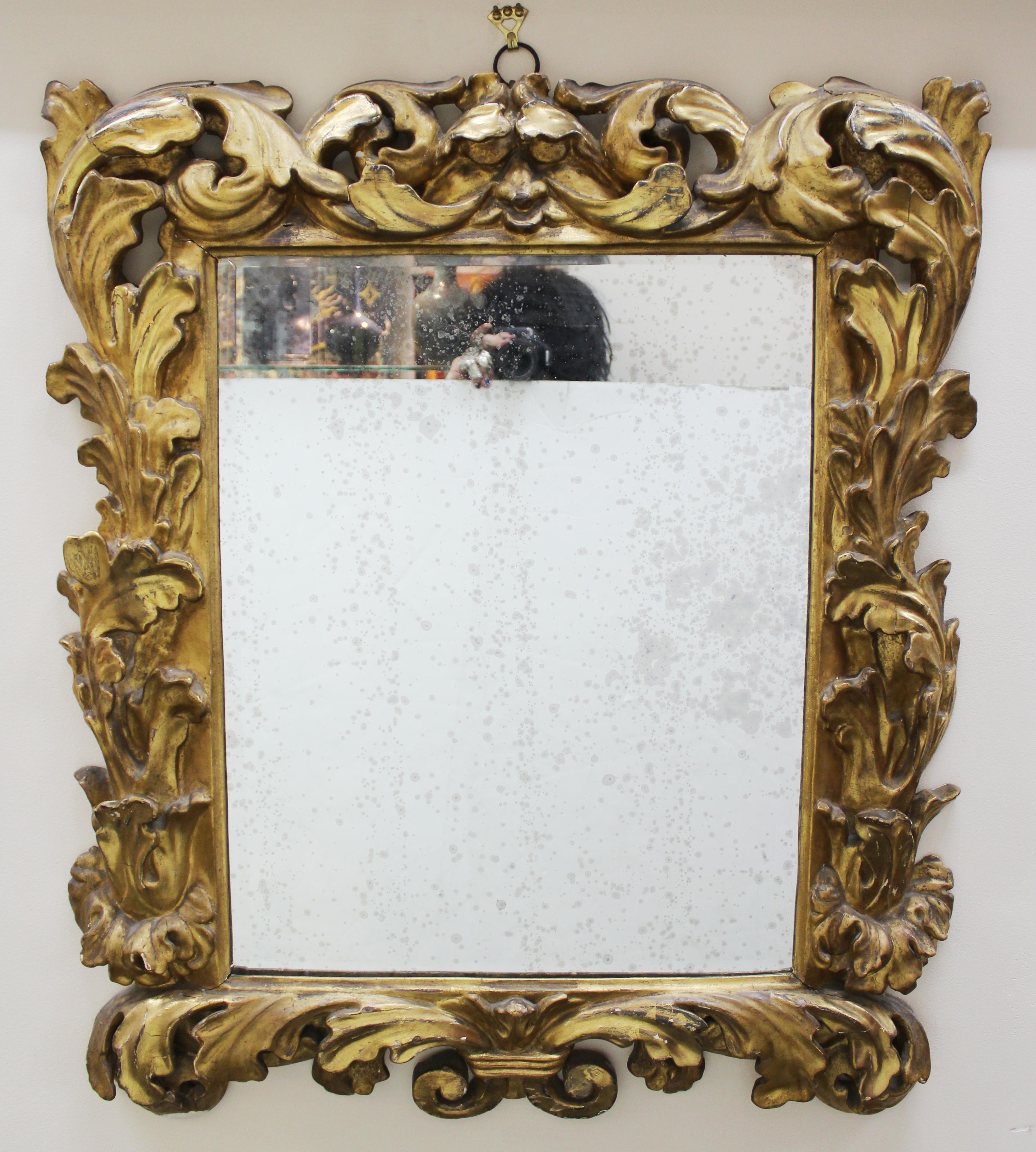 Italian Baroque giltwood wall mirror with heavily sculpted acanthus leave decor on the border and a stylized human face formed by the leaves on the central upper border. The piece was made in Italy in the 18th century and is in good antique