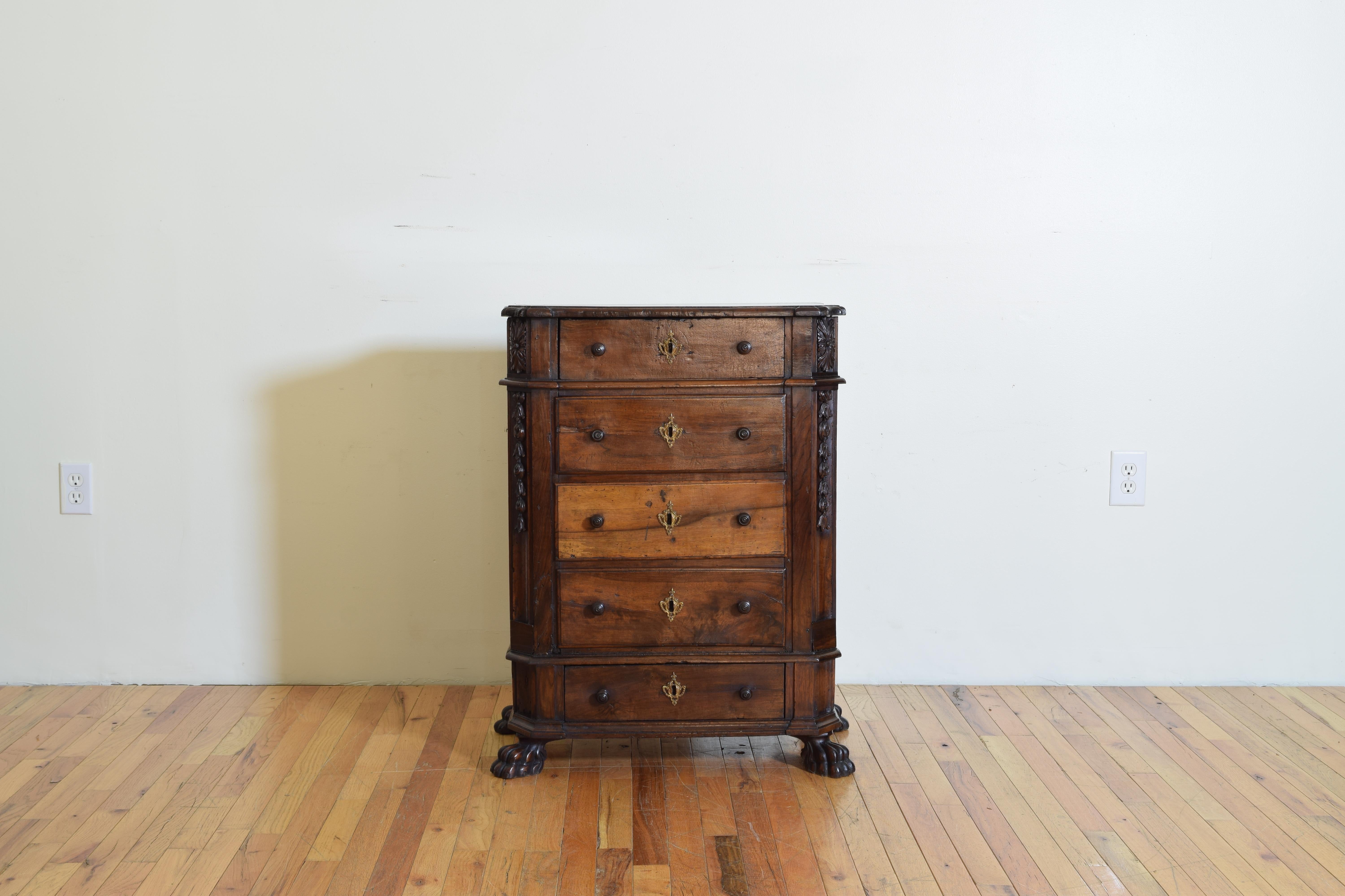 Having a shaped top with slightly flared sides and a molded edge atop a conforming case with stylized carved decorations in the upper canted corners, the case housing five drawers, raised on a plinth form base resting upon carved paw feet.