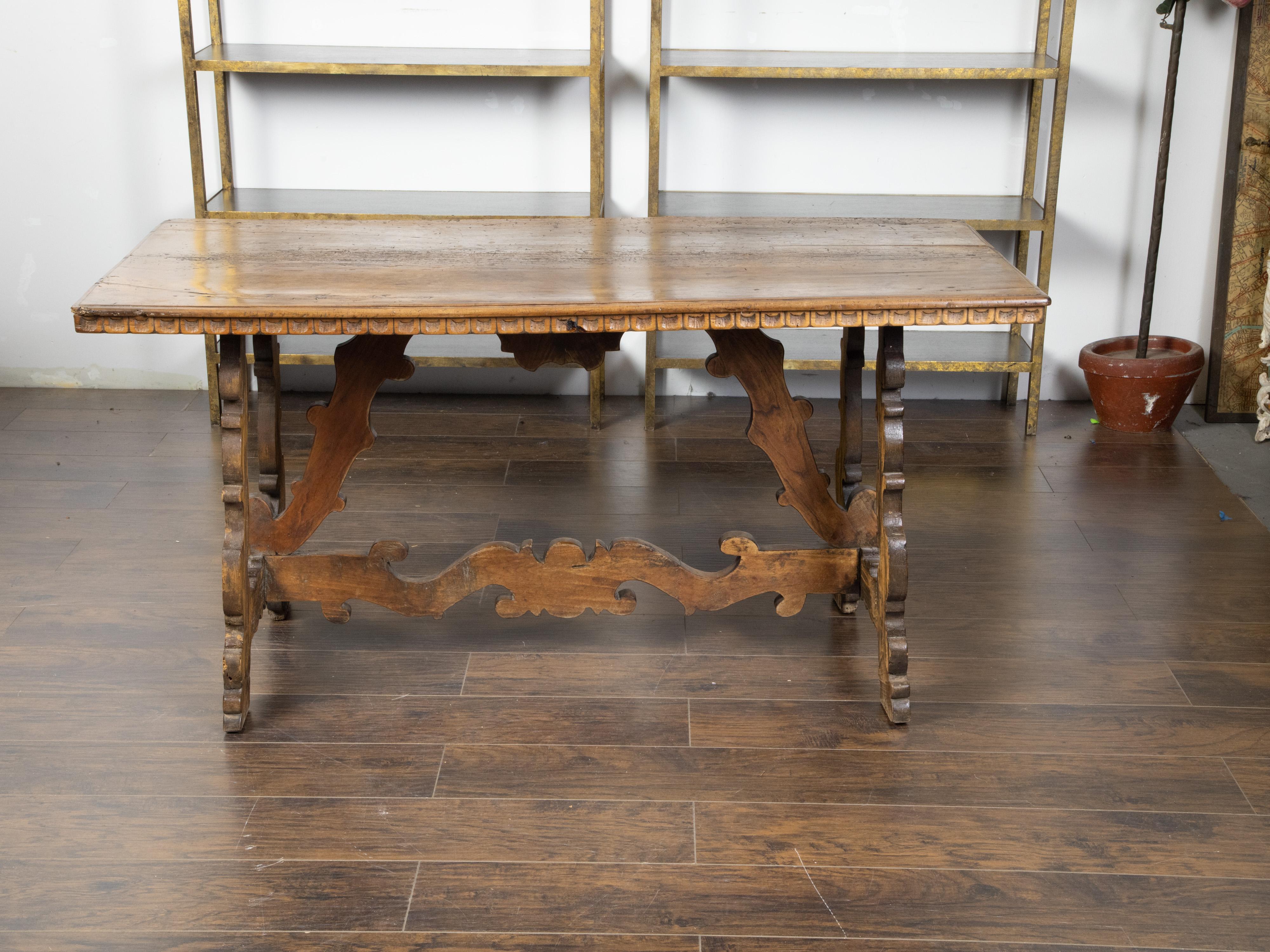 An Italian Baroque style walnut table from the 19th century, with carved trestle base and scoop motifs. Created in Italy during the 19th century, this table features a rectangular top with carved scoop motifs on the apron, sitting above an exquisite