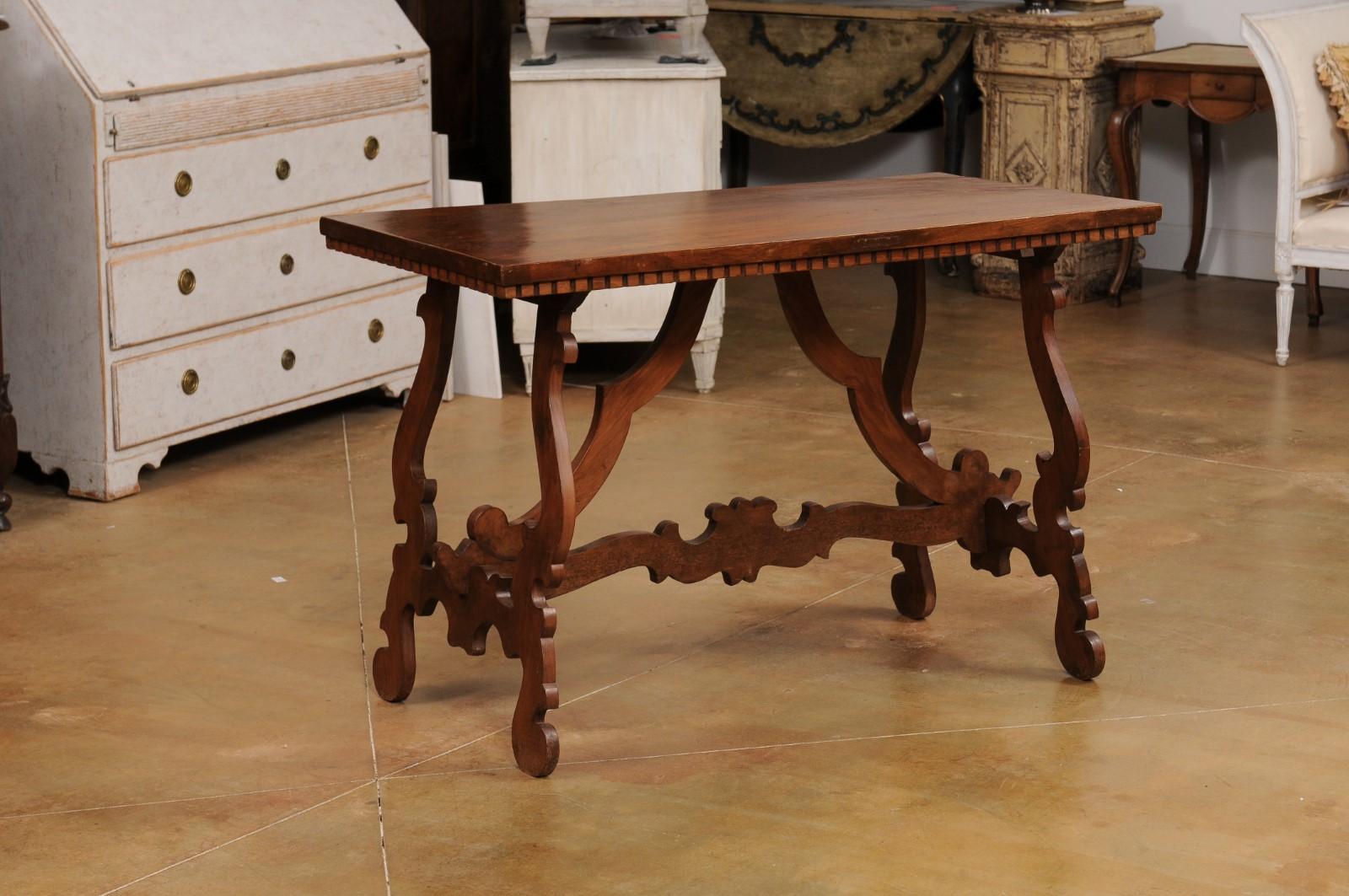 An Italian Baroque style Fratino walnut console table from the 20th century, with dentil molding, lyre-shaped base and carved stretchers. Created in Italy during the 20th century, this Fratino walnut console table features a simple rectangular top