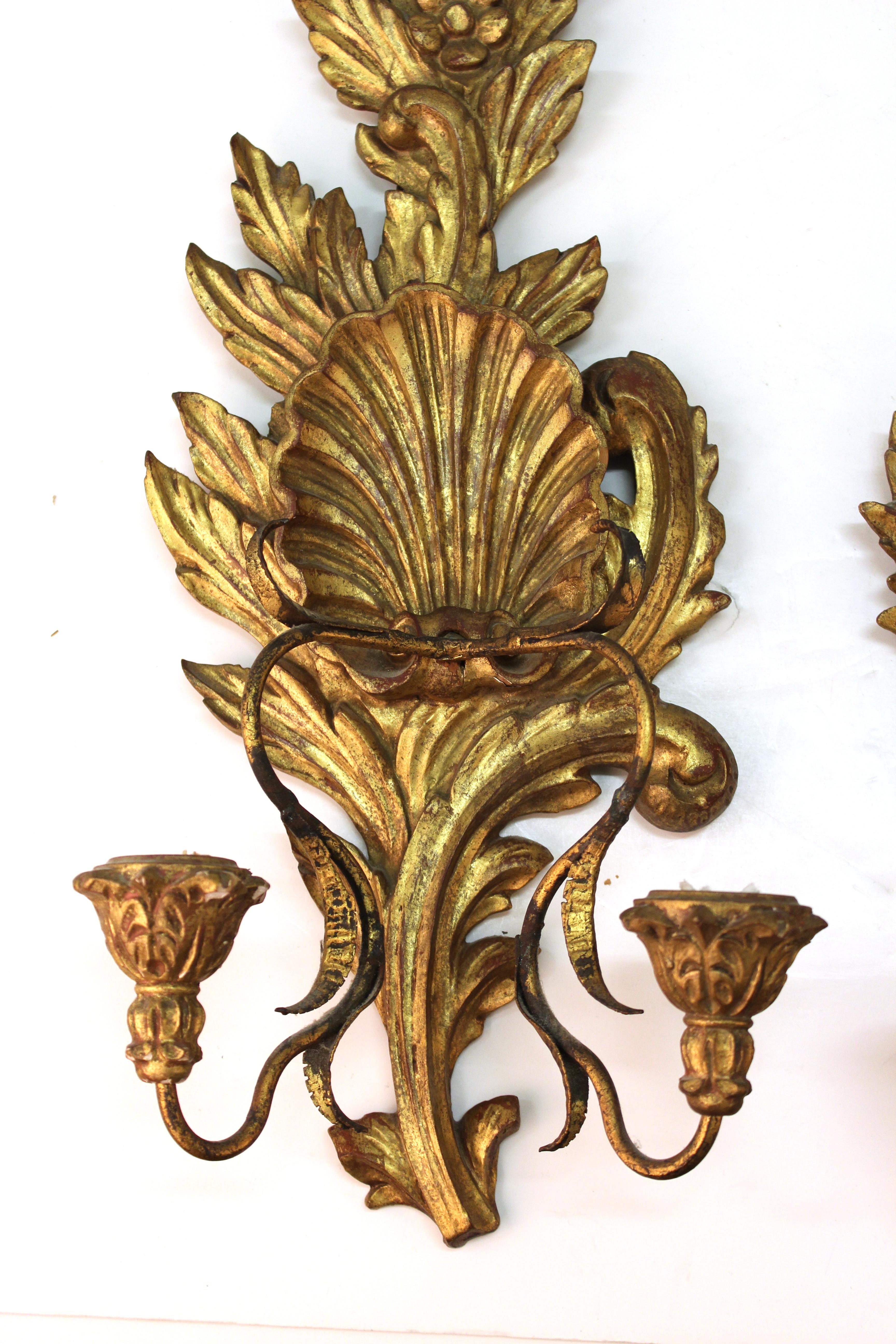 Italian Baroque style pair of wall candleholders in giltwood. Each one has scalloped shells, flowers and foliage with acanthus leaf candle cups and both backs have stamps 'Made in Italy', one with an old paper label. In good vintage condition.