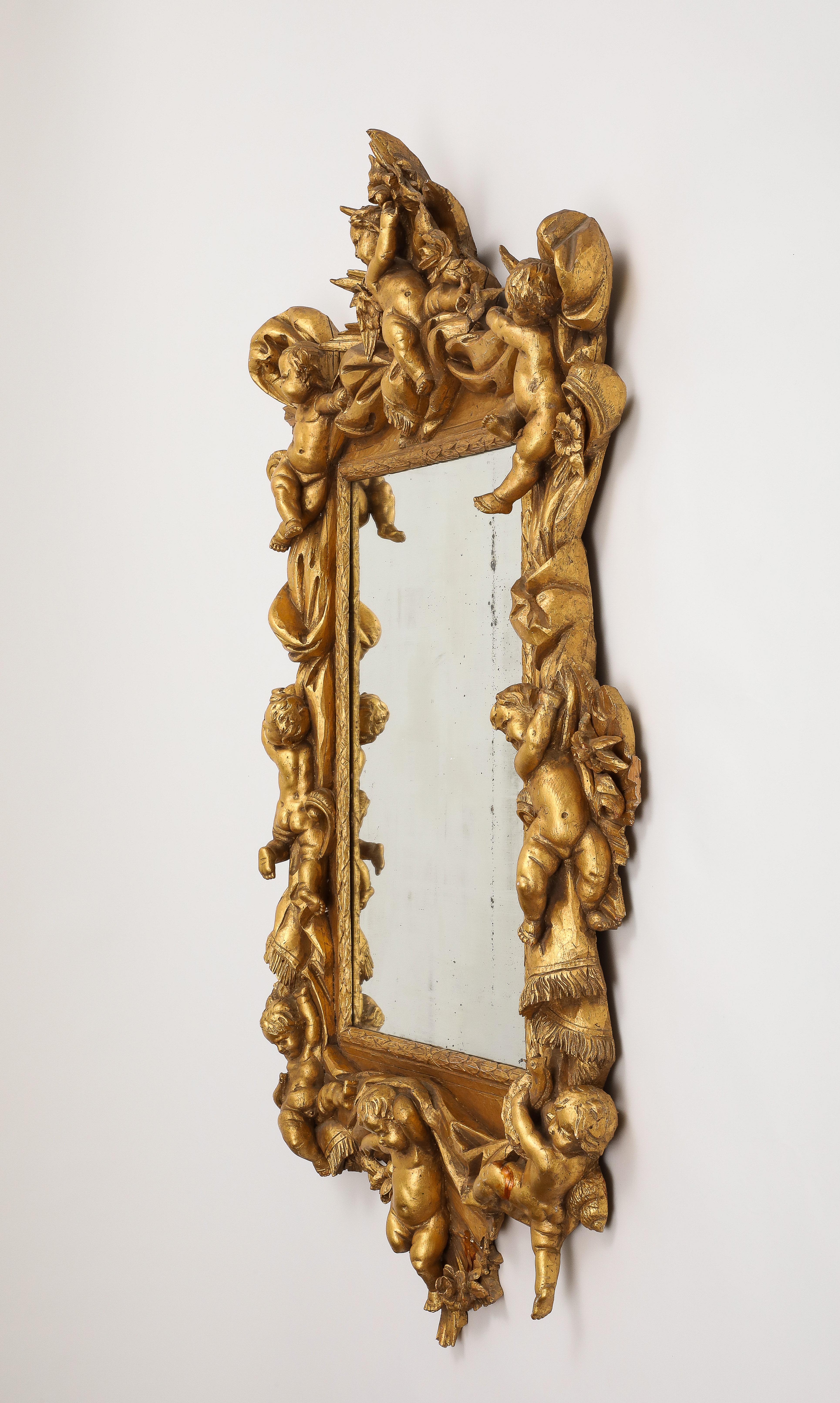 Miroir en bois doré de style baroque italien du 20e siècle, orné de fleurs et de chérubins le long d'une bordure drapée sculptée. Le fil de suspension au dos est stable et prêt à être accroché. La décoration dorée est brillante et relativement