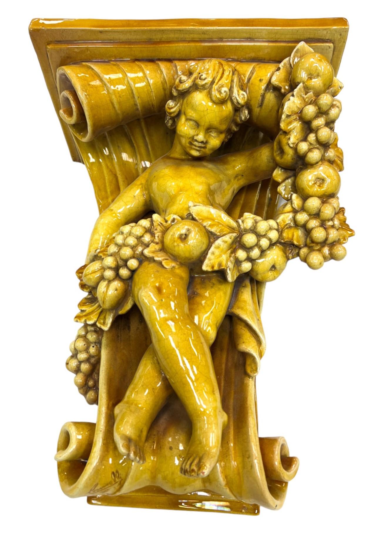 A handcrafted Italian glazed pottery putto wall bracket from the 1920s in mustard color and intricate details.

The putto, a cherubic figure holding a vine of fruits, showcases the artistry and craftsmanship of the Italian potter. The choice of