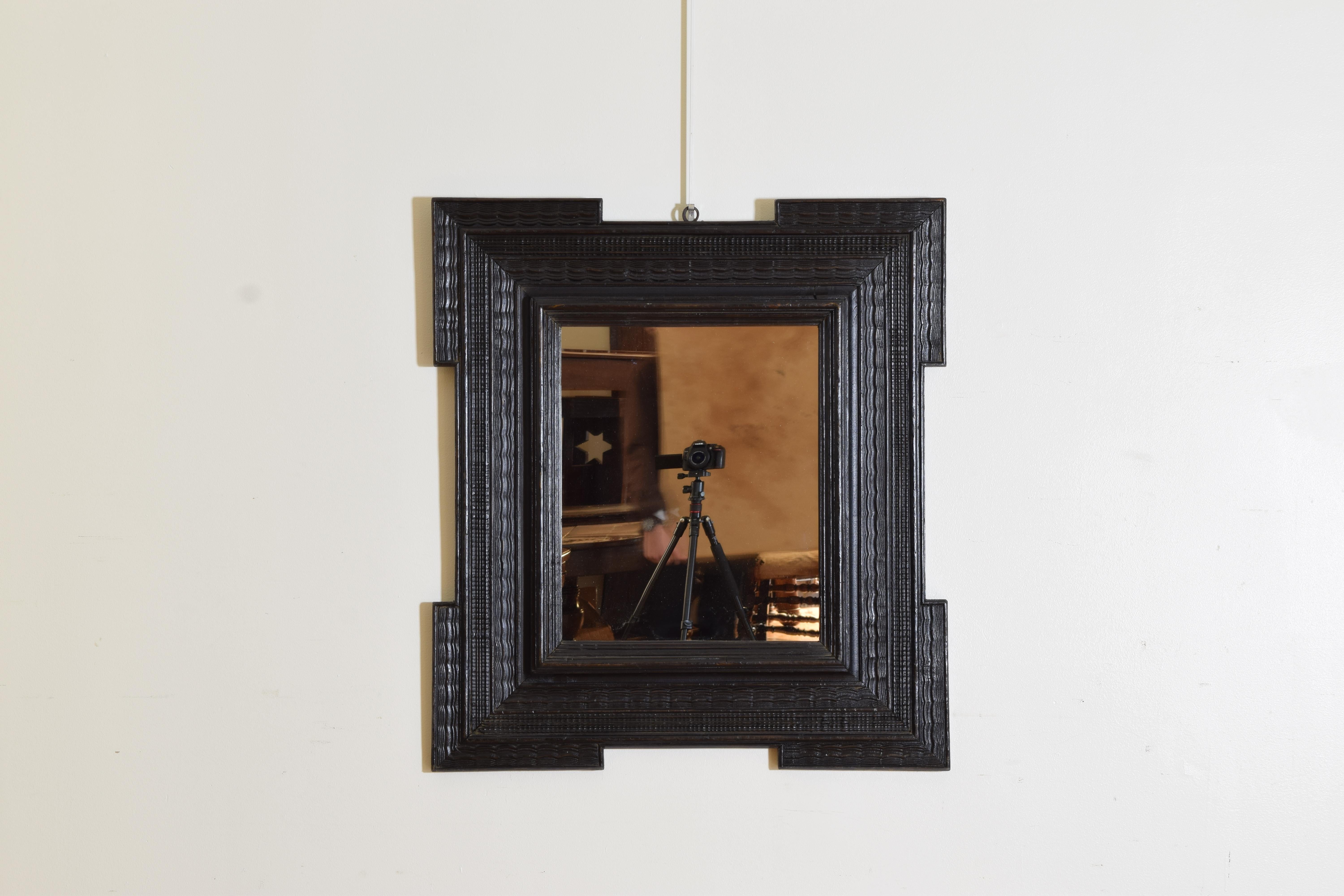 Of Northern Italian origin, a rectangular frame with notched corners and a series of molding of varying depths, guilloche carved on nearly every surface, modern mirror plate 