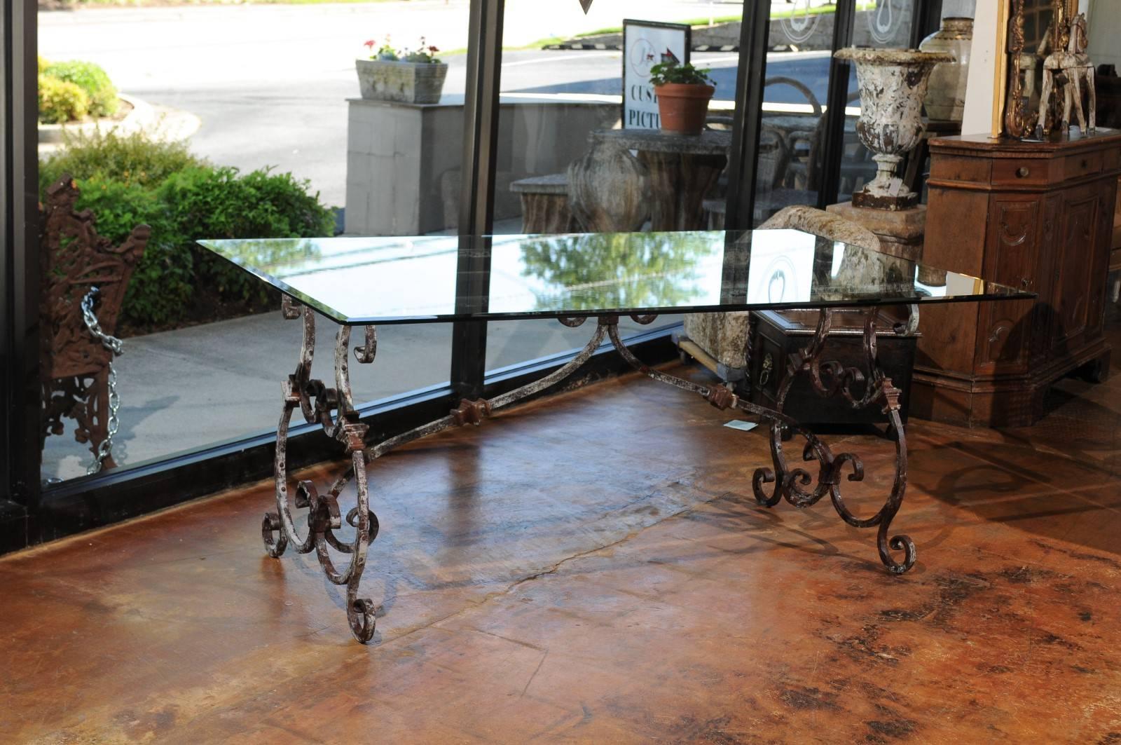 An Italian Baroque style hand-forged iron table base with lyre-shaped legs from the 20th century, with new bevelled glass top. This Italian table trestle base features two exquisite lyre-shaped legs adorned with a beautifully weathered finish,