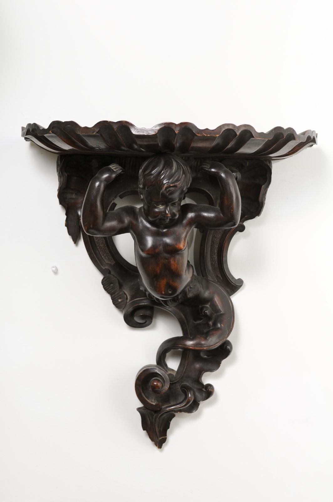 An Italian Baroque style fruitwood wall bracket from the late 19th century, with carved putto figure. Born in Italy during the later years of the 19th century, this fruitwood bracket attracts our attention with its carved putto whose body ends into