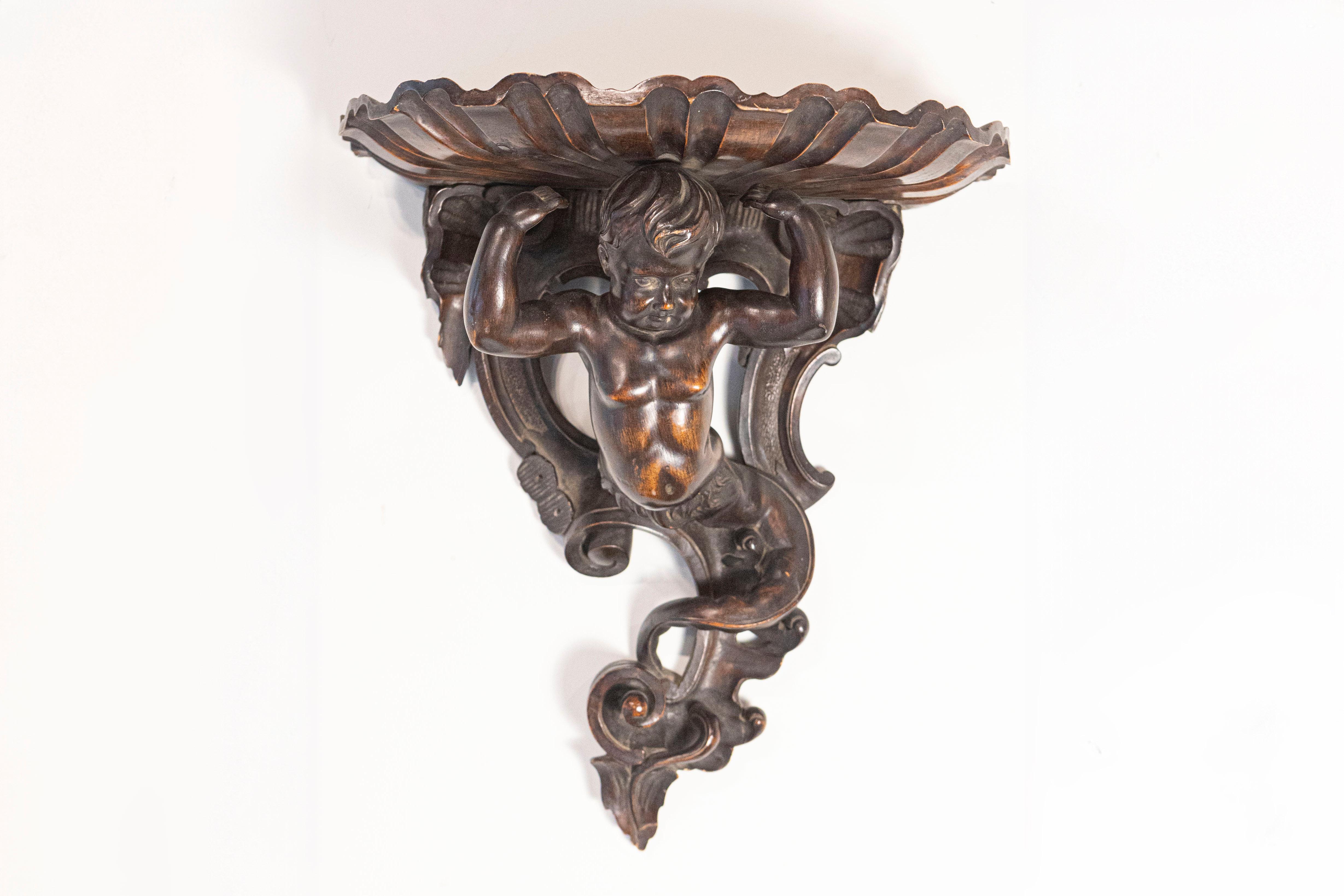 An Italian Baroque style fruitwood wall bracket from the late 19th century, with carved putto figure. Born in Italy during the later years of the 19th century, this fruitwood bracket attracts our attention with its carved putto whose body ends into