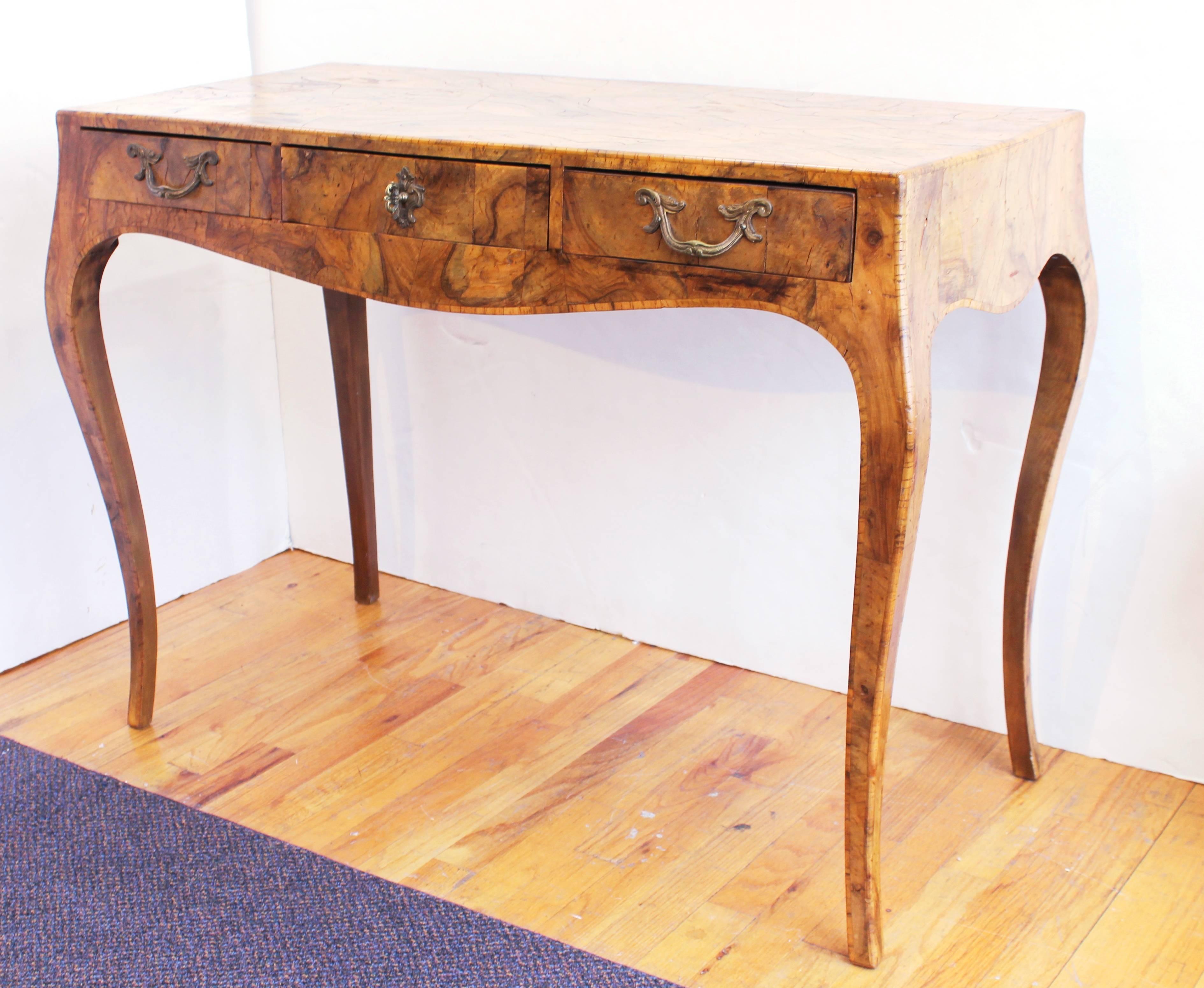 Italian Baroque style oyster burl wood console table with cabriole legs, bombe sides and three drawers. The piece has some natural cracking to the wood finishing and minor stress cracks but is in overall good vintage condition.