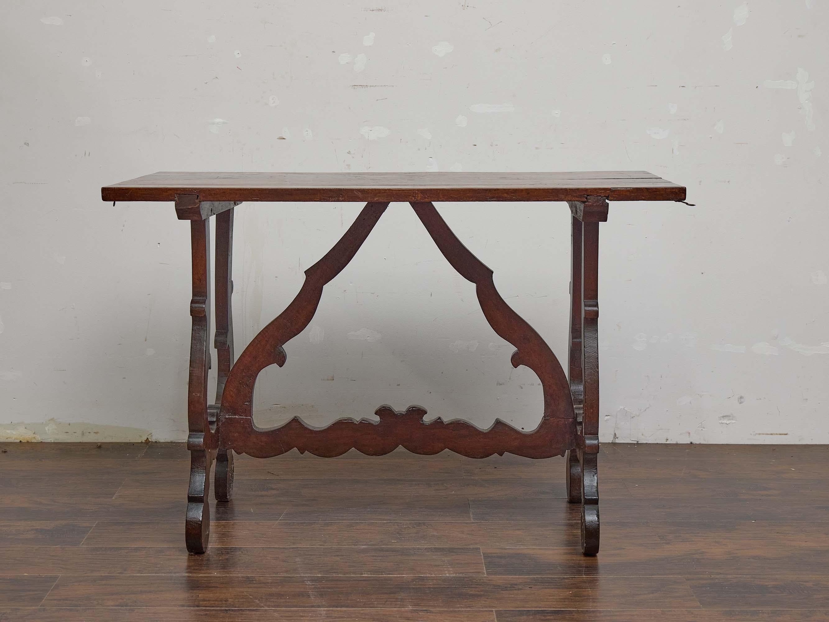 Crafted in Italy circa 1800, this walnut console table reflects the enduring influence of the Baroque style, with its sculptural silhouette, boldly scrolling legs, and shaped stretcher. The top is composed of a thick walnut plank, with a secondary