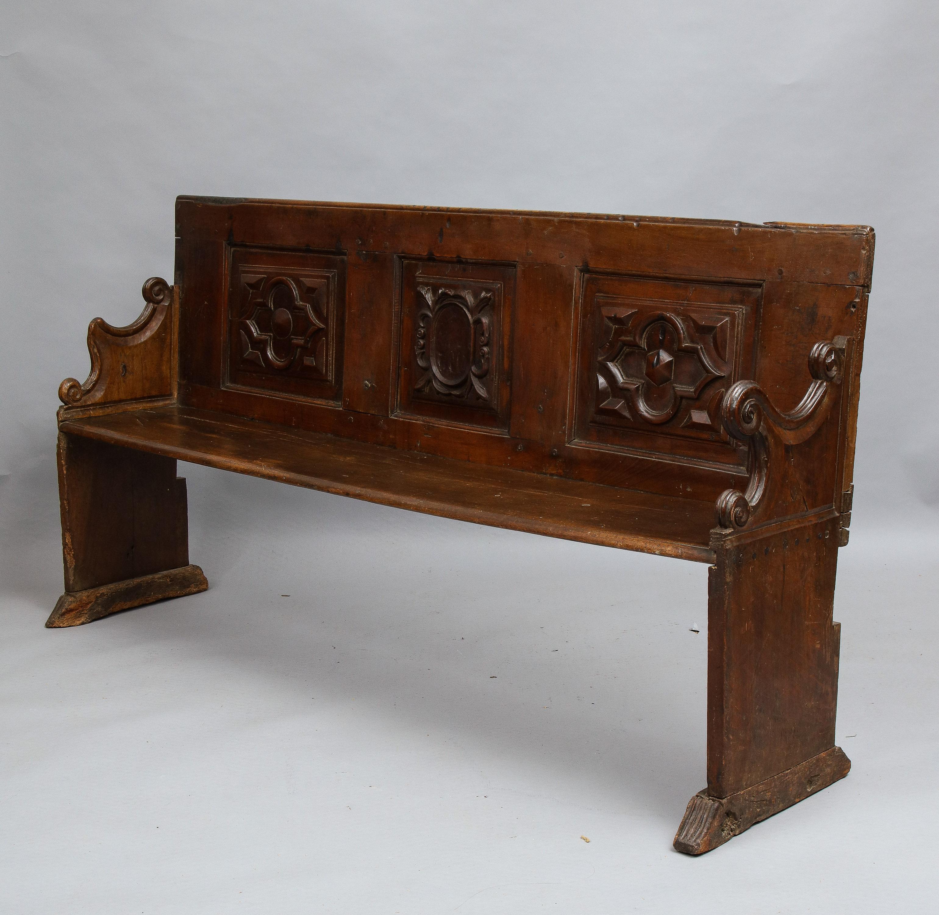 A good late 17th Italian walnut bench, the paneled back with molded edge, the three panels with geometric carved relief, the slab sides with richly scroll carved arm supports, standing on shoe feet with ribbed carved toes, the whole with pleasing