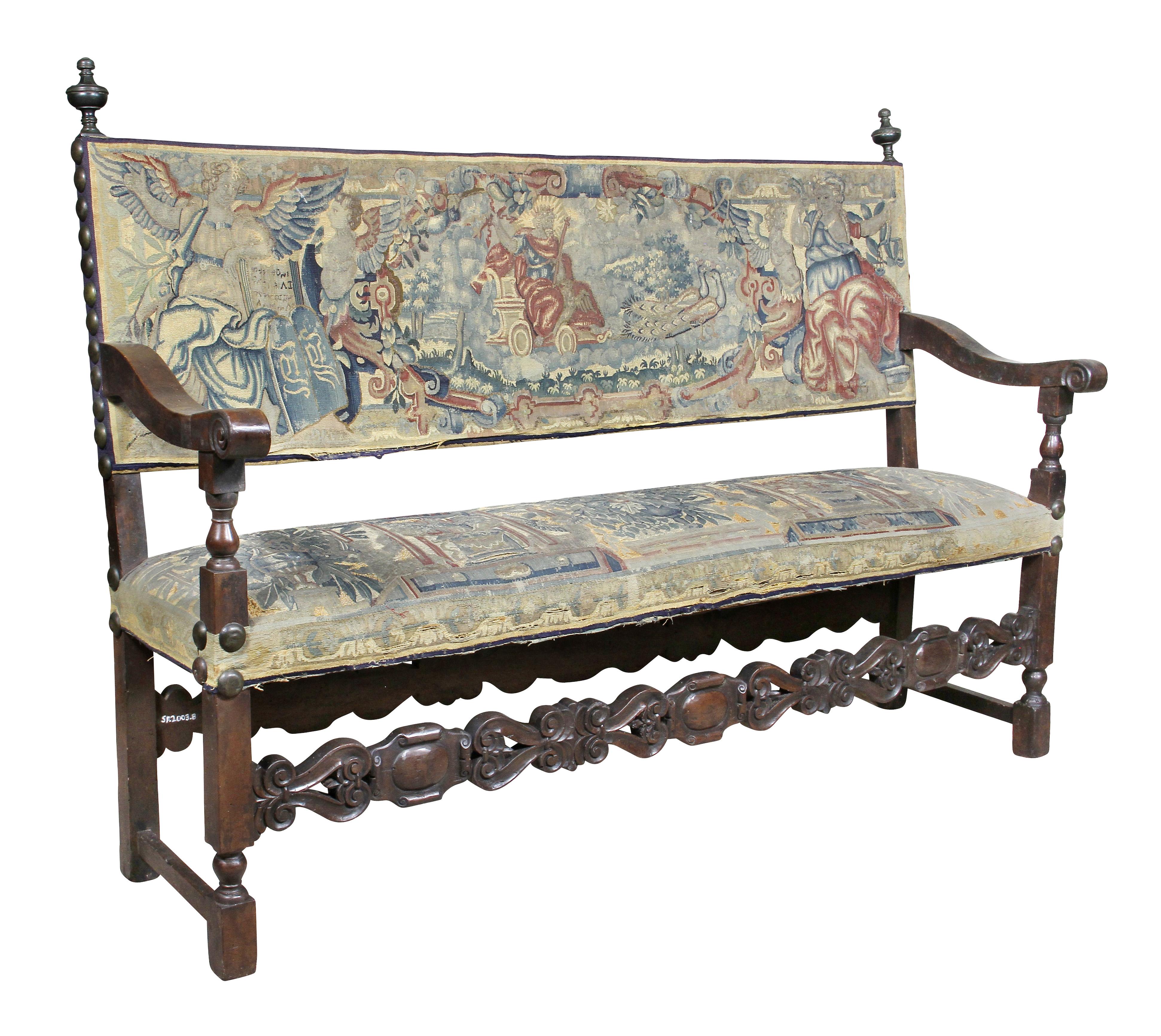 With rectangular back with bronze finials, arms with carved hand holds and supported on turned supports, rectangular seat raised on square section legs joined by a carved stretcher. Upholstered in early 18th century Flemish tapestry. Provenance,