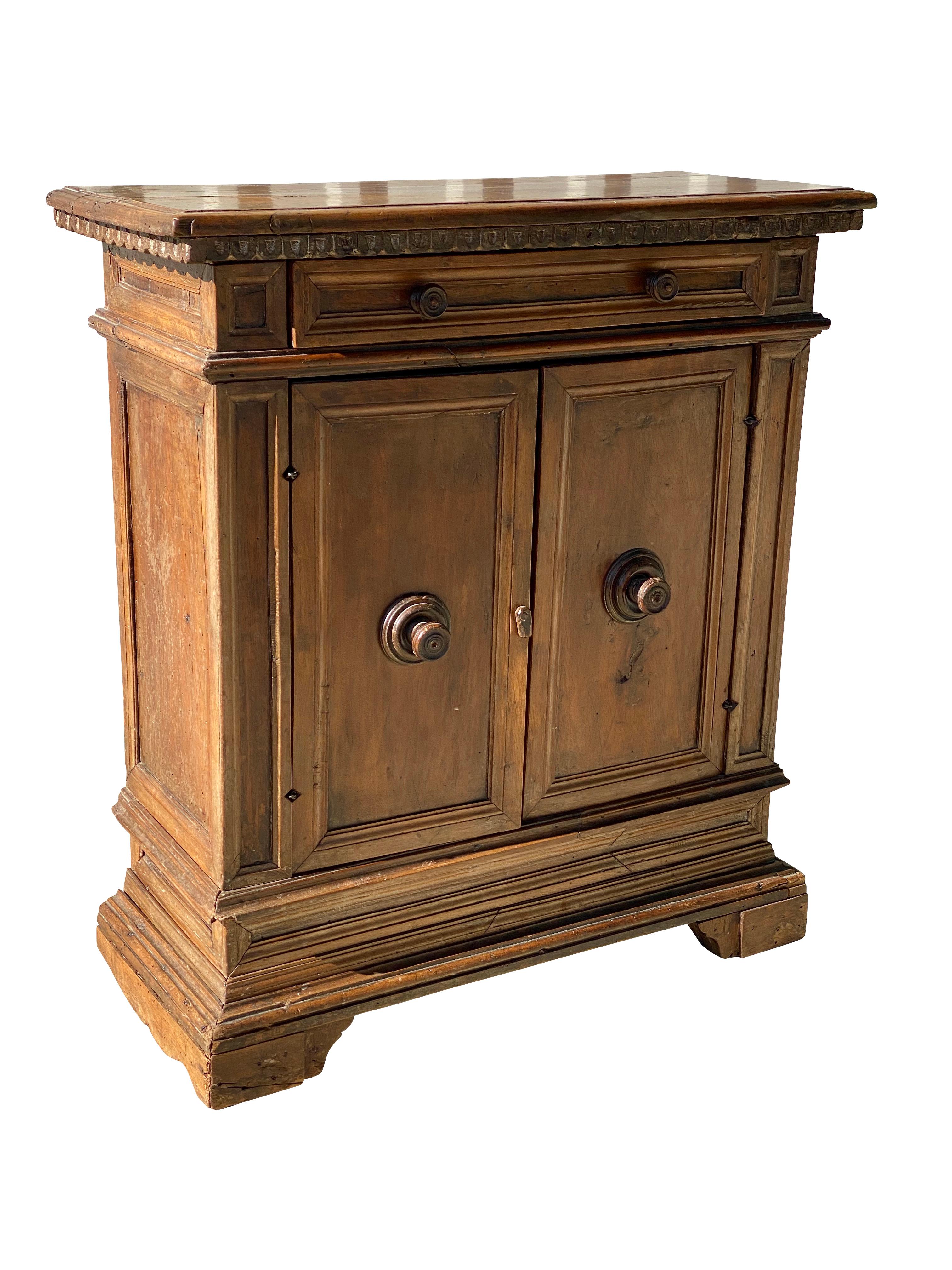 Rectangular top over a carved applied edge over a drawer and pair of cabinet doors with wood handles, bracket feet.