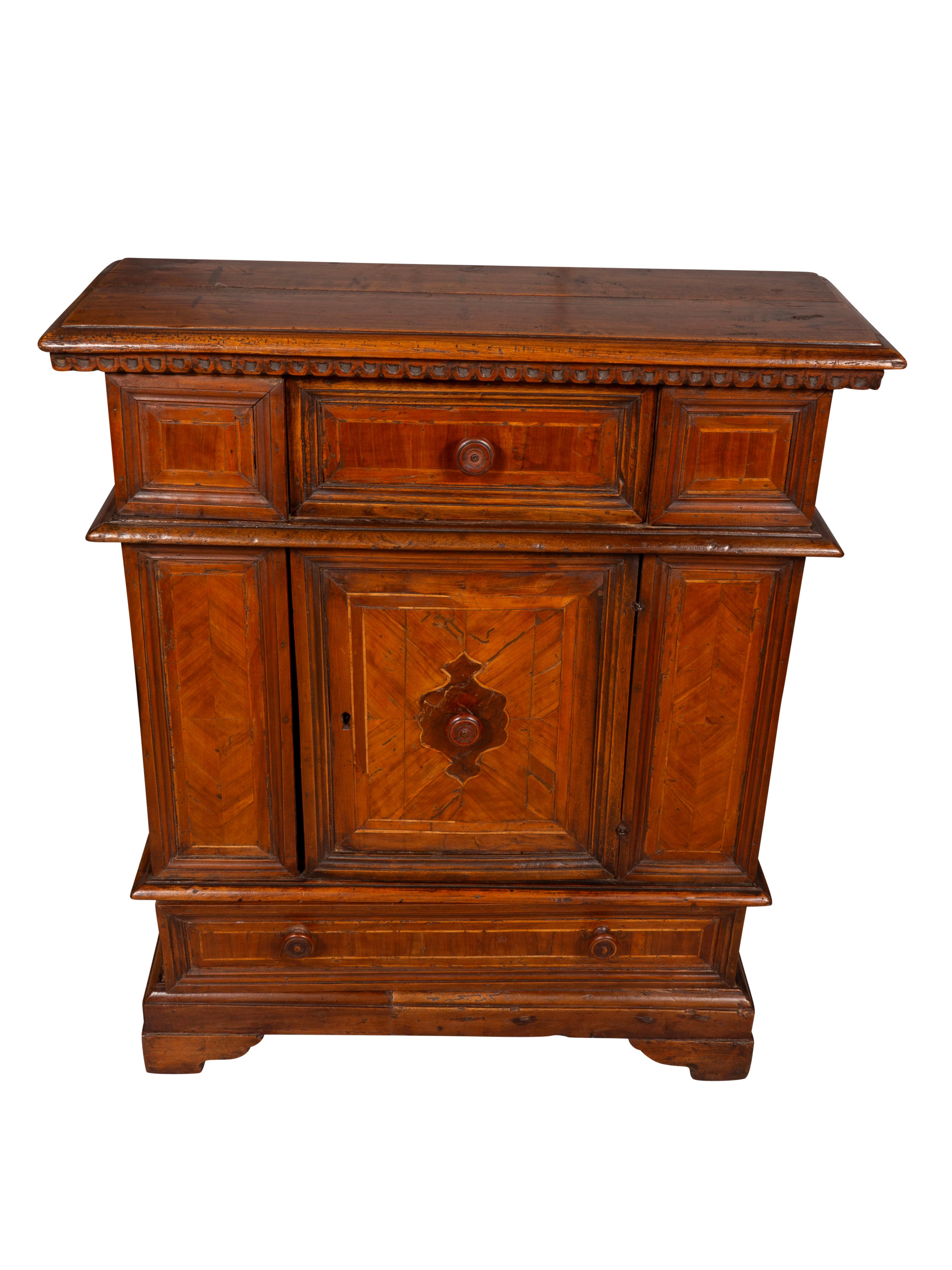 With a rectangular top over a drawer and a door and a lower drawer. Bracket feet.