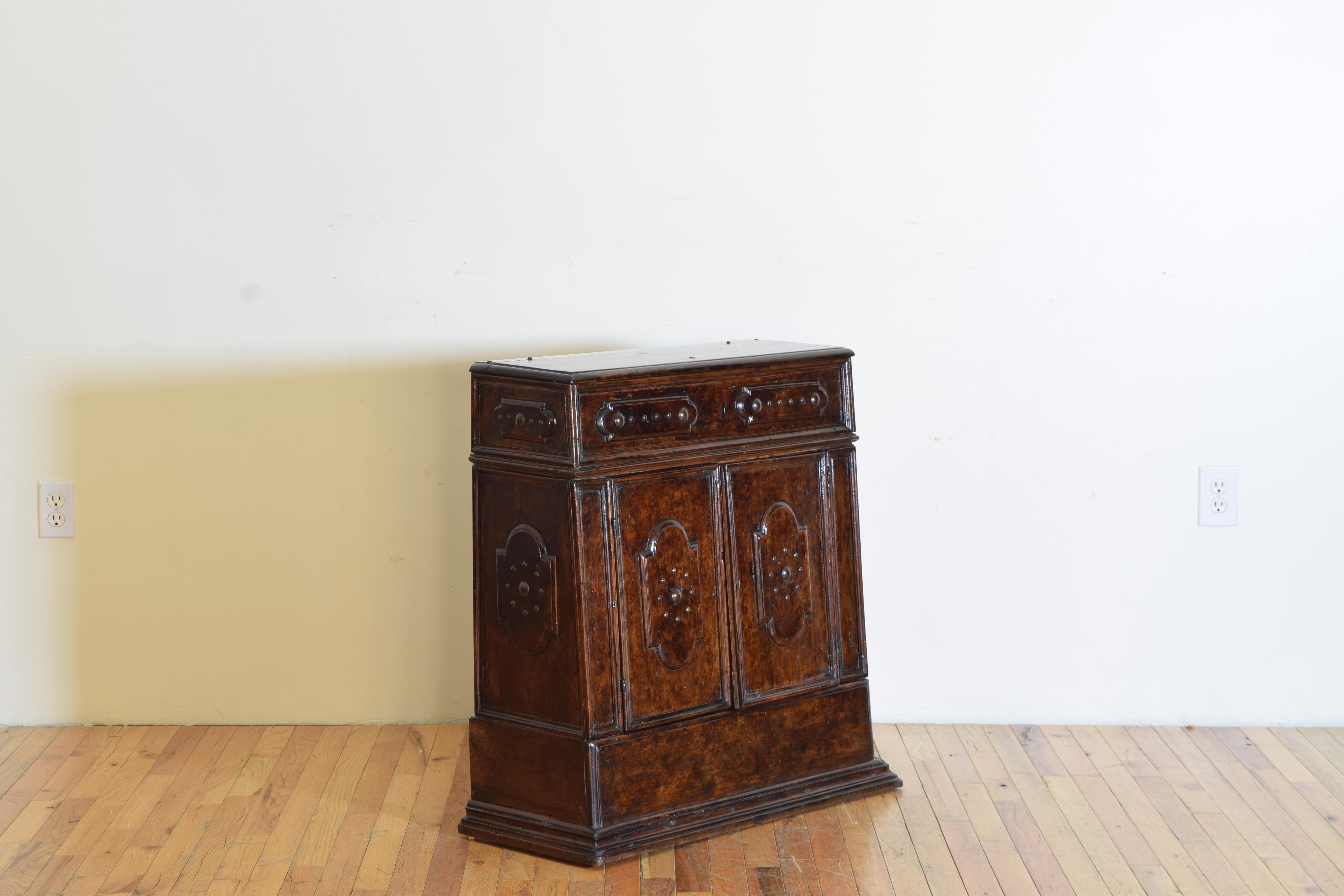 Having a hinged rectangular top above a conforming case that tapers up to a more shallow depth, the case with two drawers and raised on a plinth-form base, decorated with patinated brass nailheads.