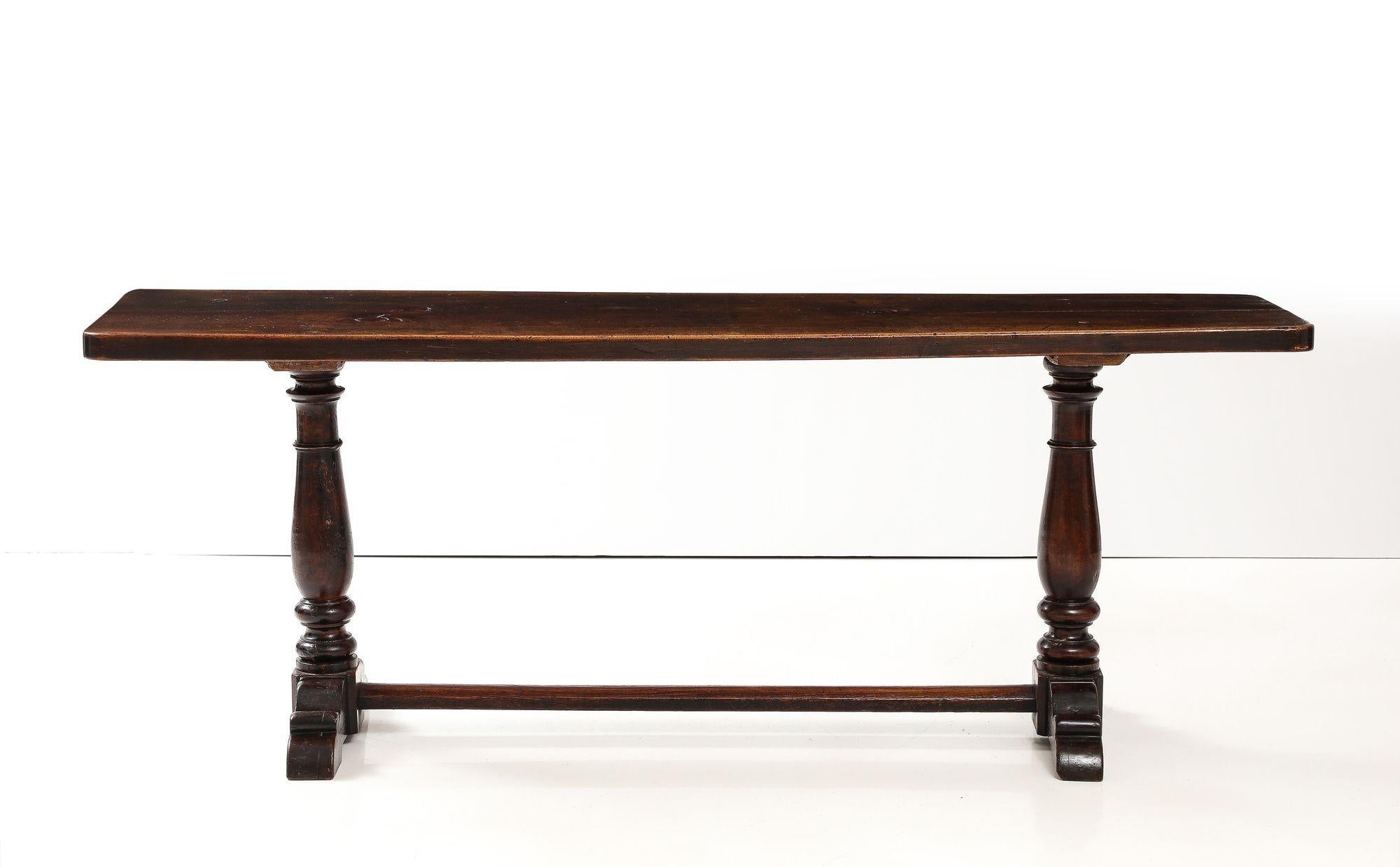 Fine Italian baroque walnut trestle table, the bold top fashioned from a single plank, standing on balustrade-turned trestle ends joined by bar stretcher over sled feet, the whole with good rich nutty color and even patination.