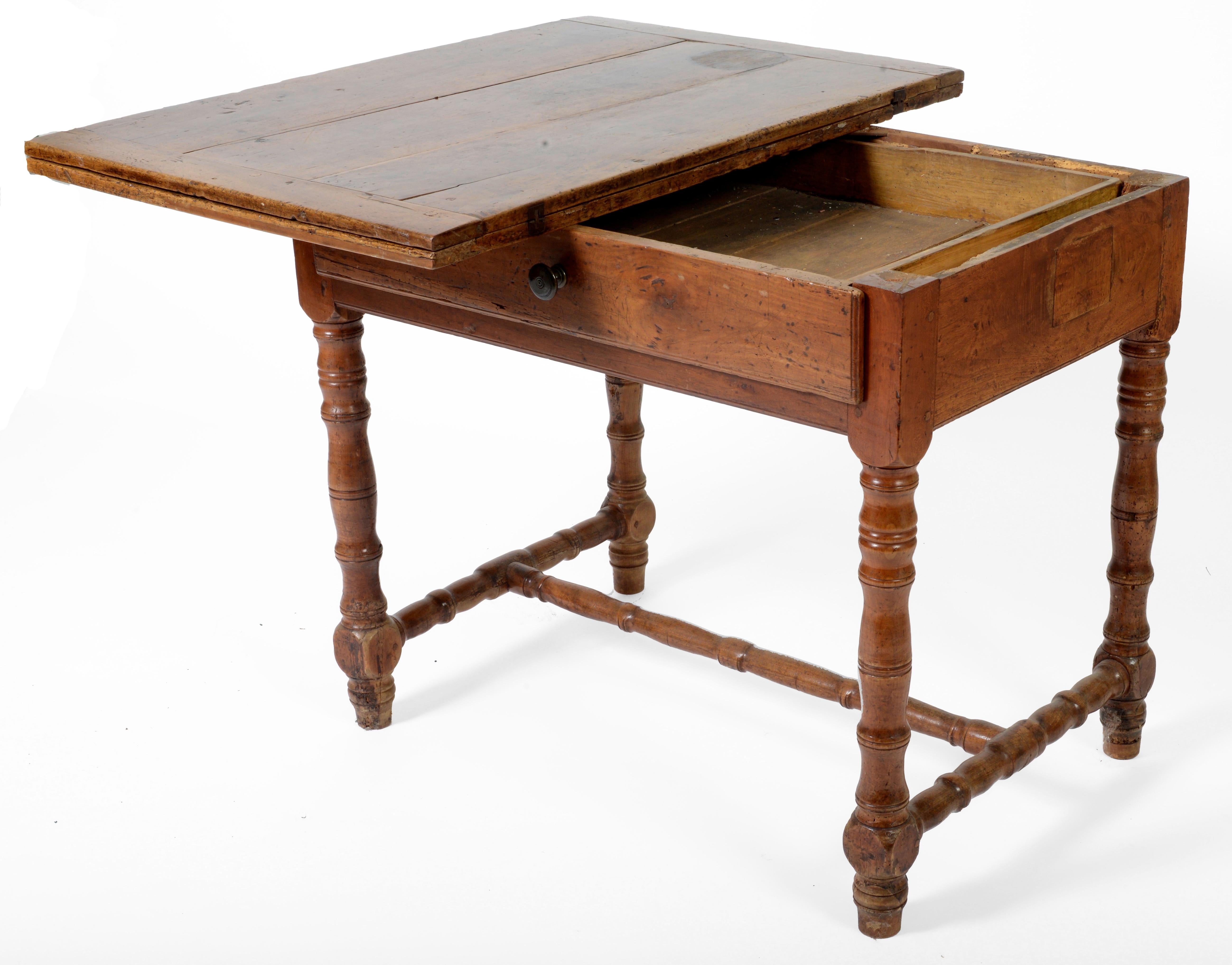 An Italian Baroque walnut writing table with unique hinged top, the rectangular top with bread boarded ends, opening and turning to create a large writing surface, the frieze containing a central drawer, raised above ring turned legs and “H”