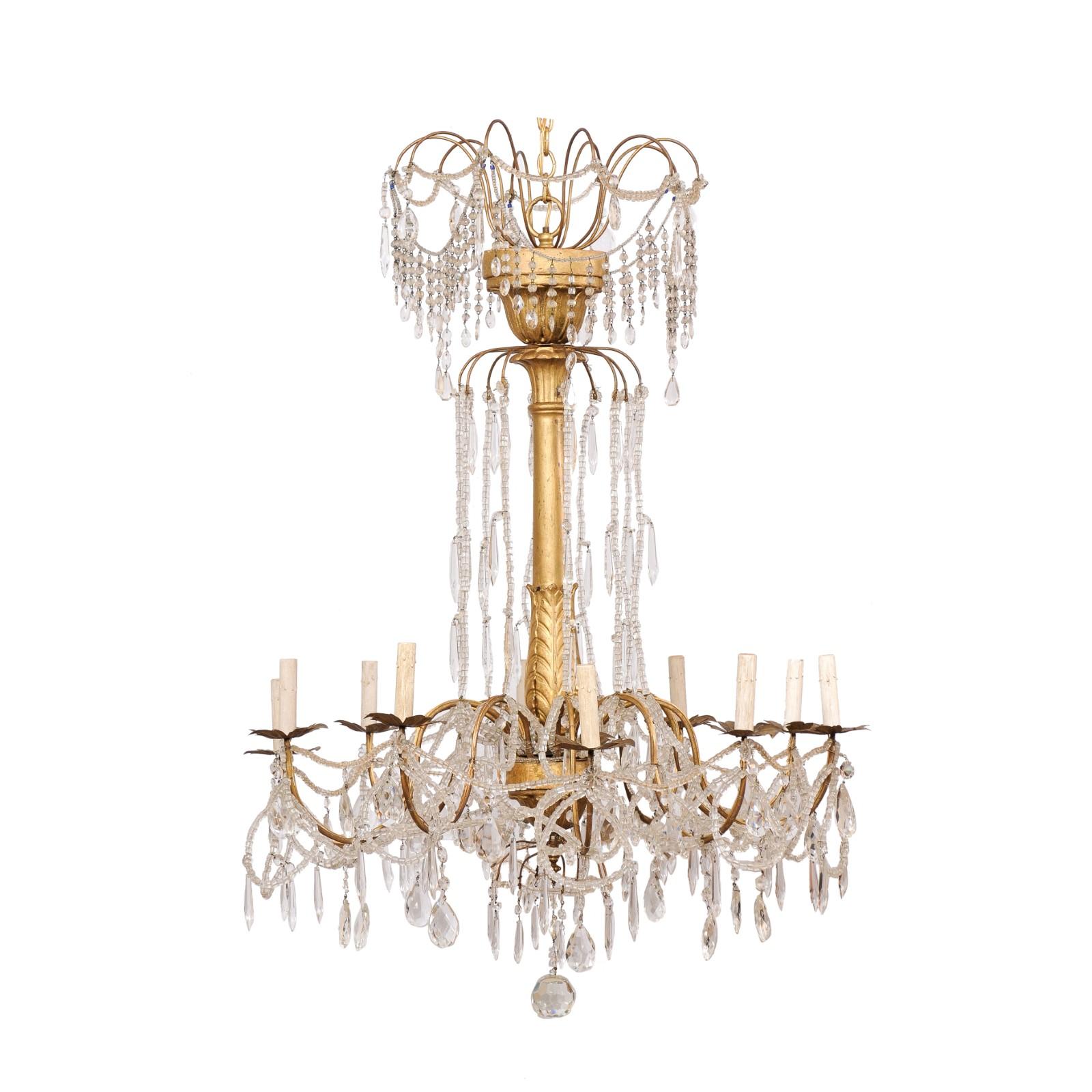 An Italian crystal and gilt wood column chandelier from the mid 20th century. This mid-century hanging light from Italy features a gilt-wood central column, adorn with leaved-wraps carved about it's lower gallery and floral wraps about the top and