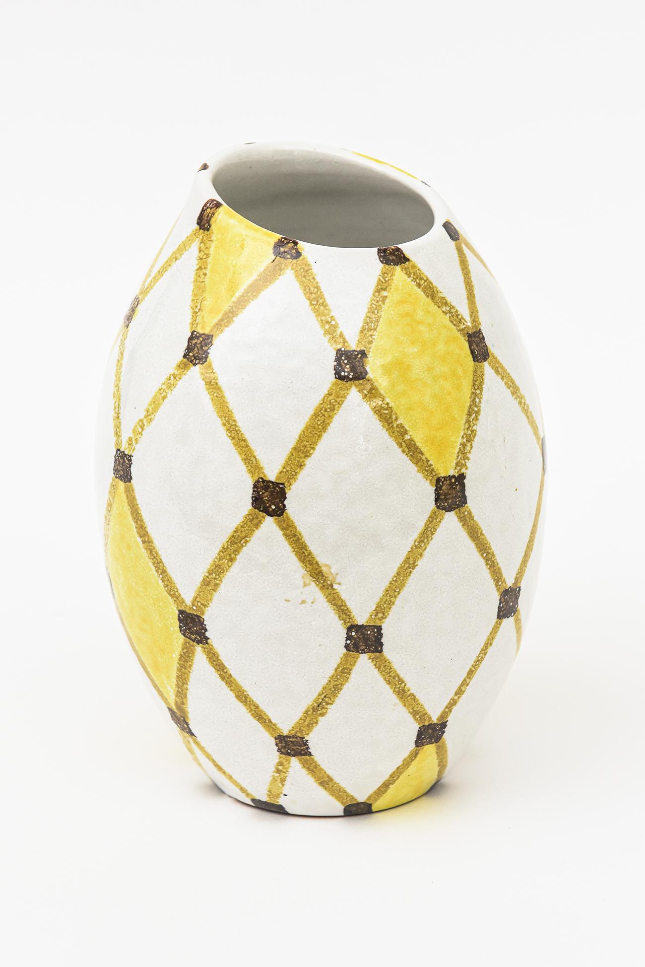 This unique and unusual vintage painted ceramic Italian Bitossi vase or vessel or object is marked with numbers on the bottom and reads V412/016 and a signature not legible. The design is diamond patterned and the colors are yellow, white, brown