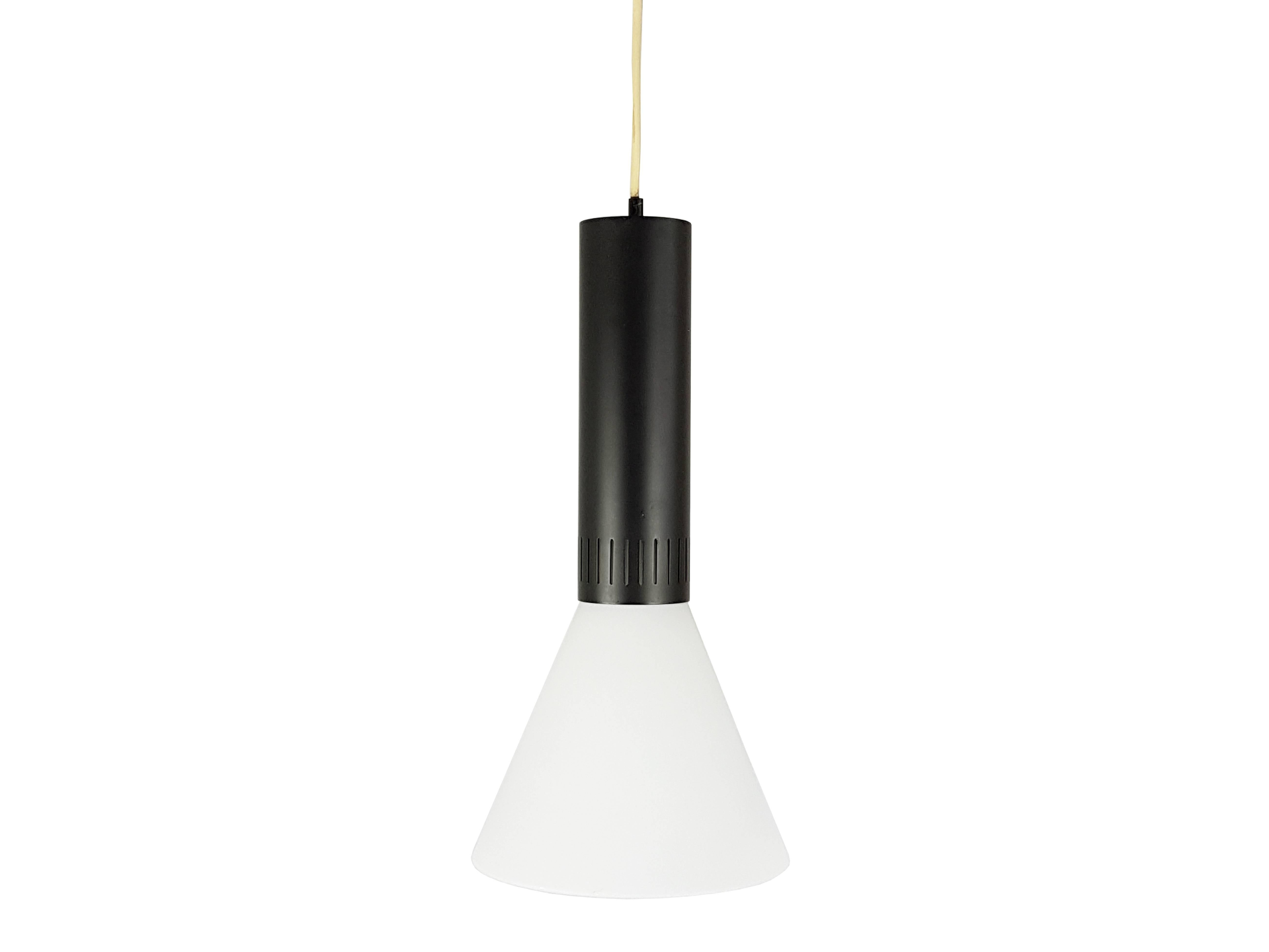 This pendant lamp model 1135 was designed and produced in Italy by Stilnovo the late 1950s. It is made from a cylindrical black lacquered metal shade holder, and a shaped white opaline glass shade. The lamp is completely original and remains in very