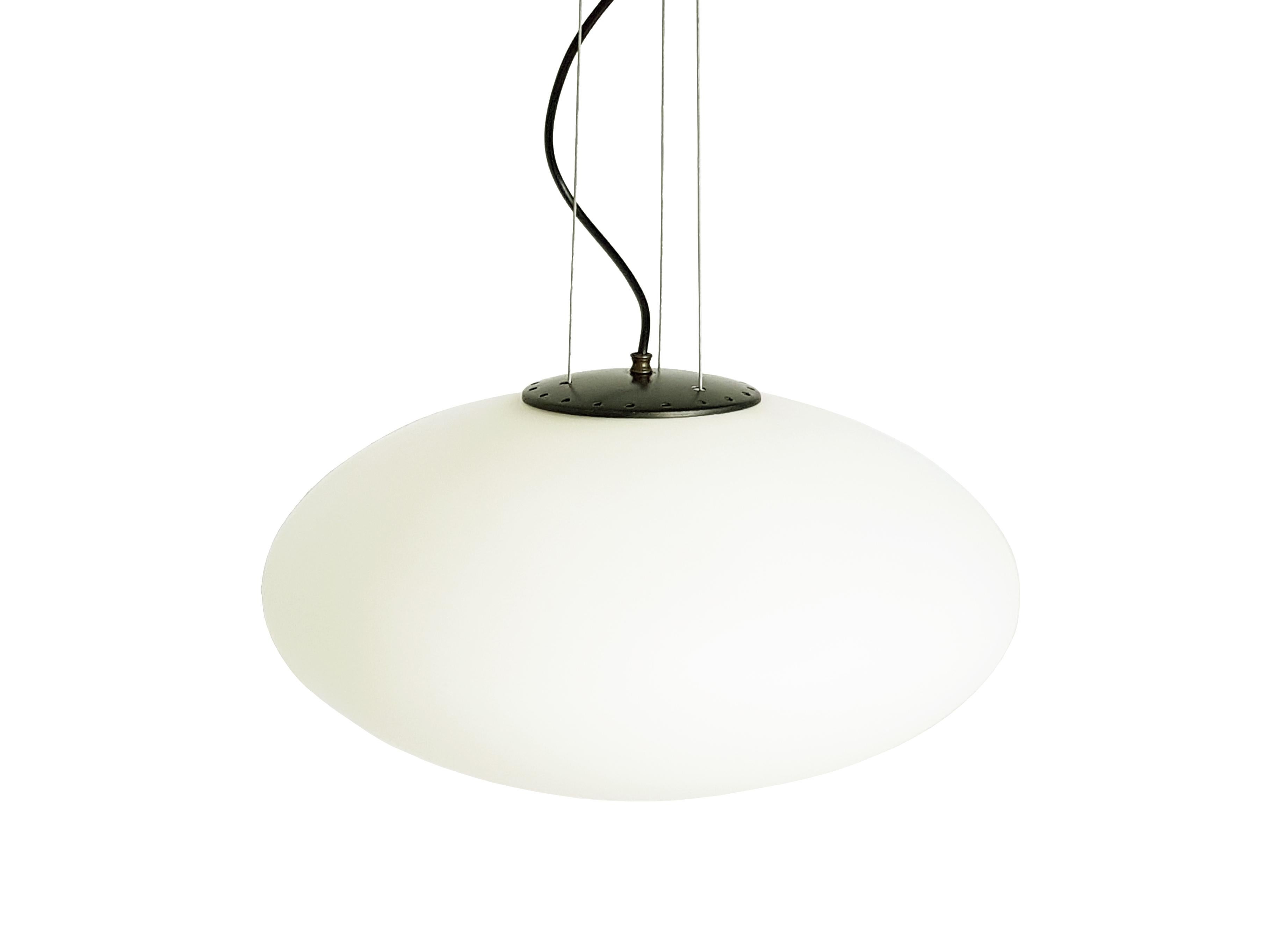 This Italian pendant was produced around the 1960s in the style of Stilnovo.
It is made from a white oval glass sandblasted shade with black metal and brass ceiling and cover. The lamp is equipped with one light socket (E27 standard) and remains in