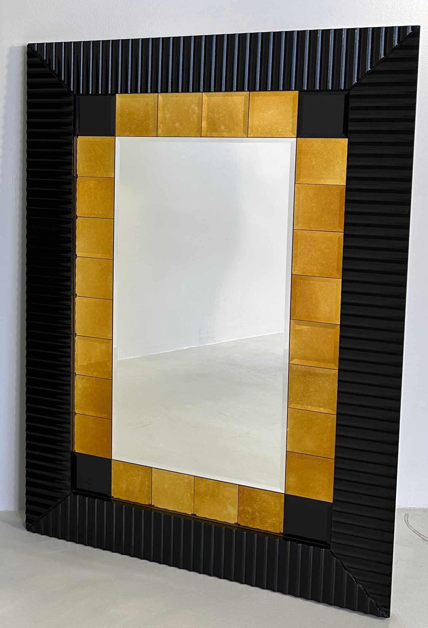 This mirror was produced in Italy in the 1980s. 
The frame is in black lacquered worked wood, the internal frame is composed by 4 black squared glasses and 24 gold squared mirrors. All the glasses and mirrors are bevelled.