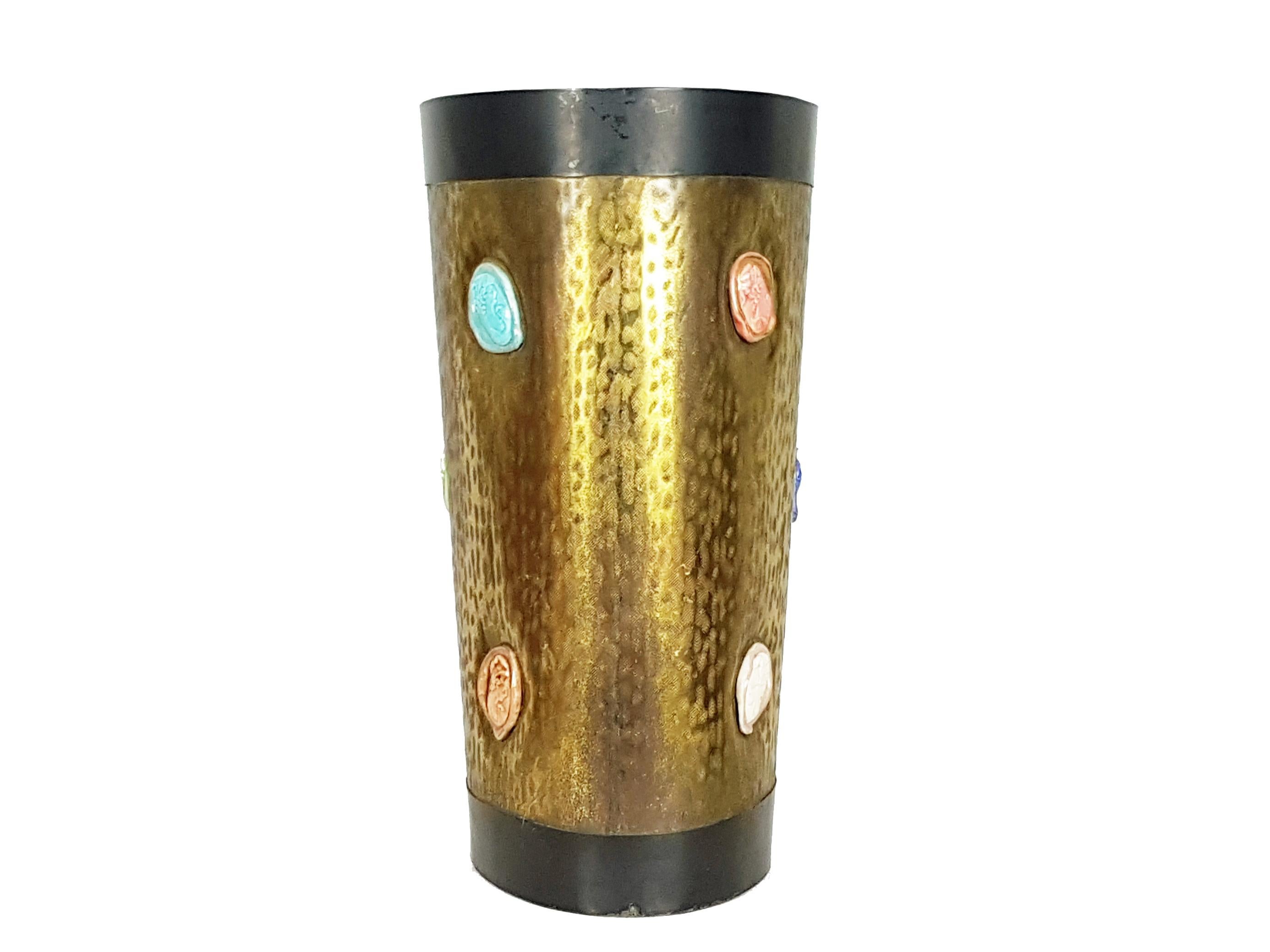 This elegant umbrella stand was manufactured in Italy in the 1950s.
It is made from an engraved brass sheet with two black painted metal stripes and multicolored ceramic 