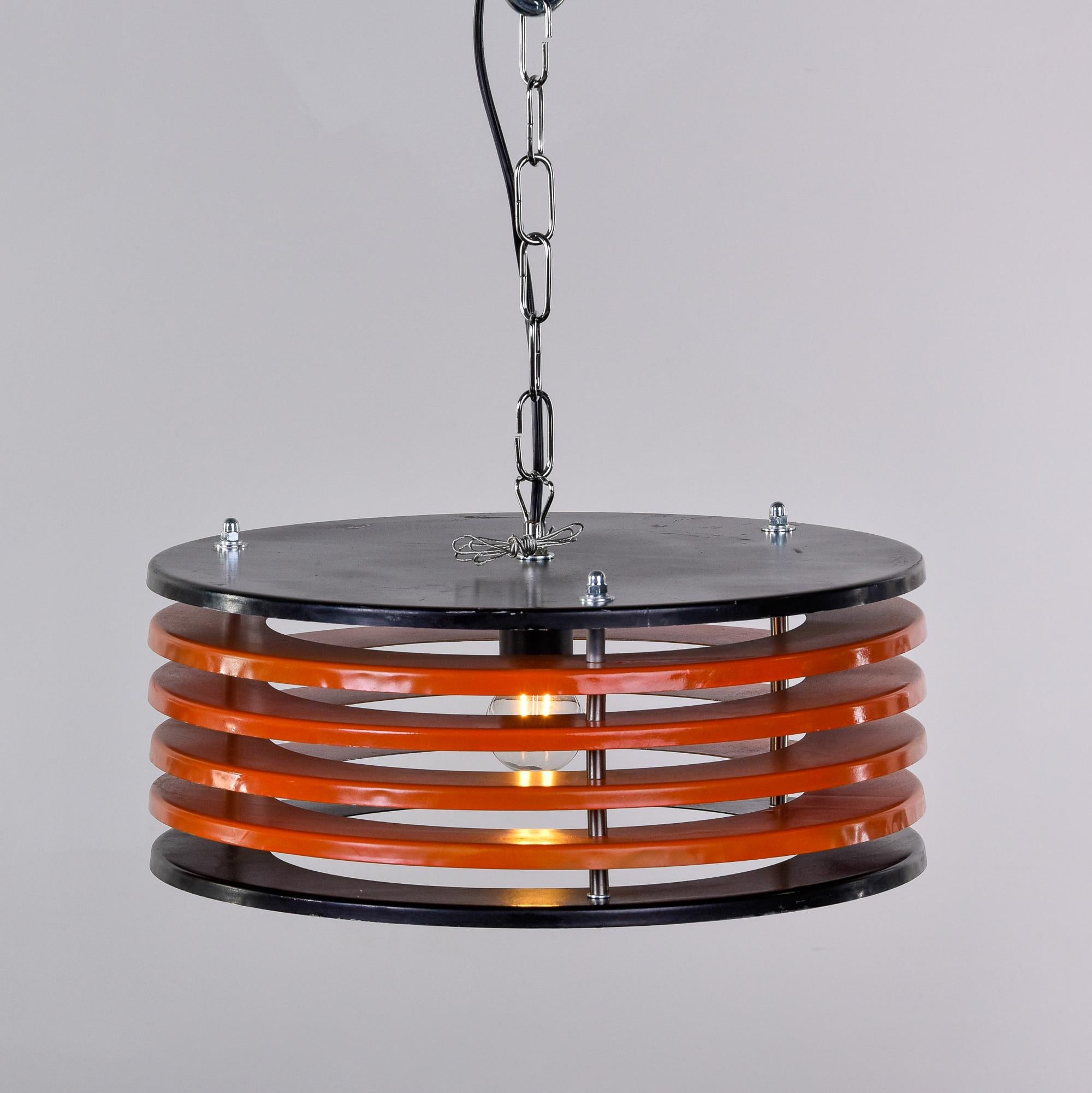 Found in Italy, this mid-century metal pendant light dates from 1970. This fixture has a single, standard sized socket and round shaped frame that has a black top and bottom with stacks of four orange disks between. Unknown maker. New wiring for US