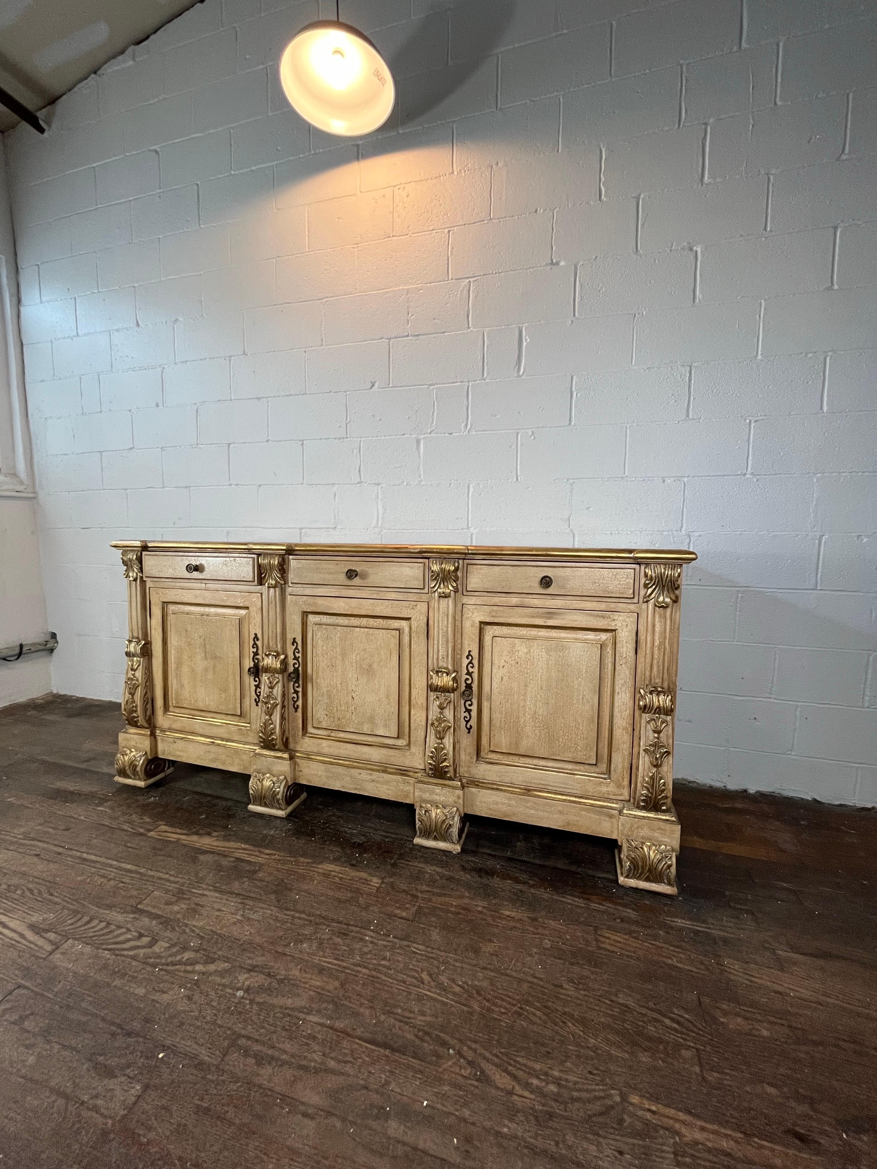 Precioso aparador o buffet grande de estilo italiano. Toneladas de almacenamiento con 3 puertas para exponer estanterías, junto con 3 cajones superiores profundos. Bien detallado con acento de acanto dorado. Aspecto envejecido