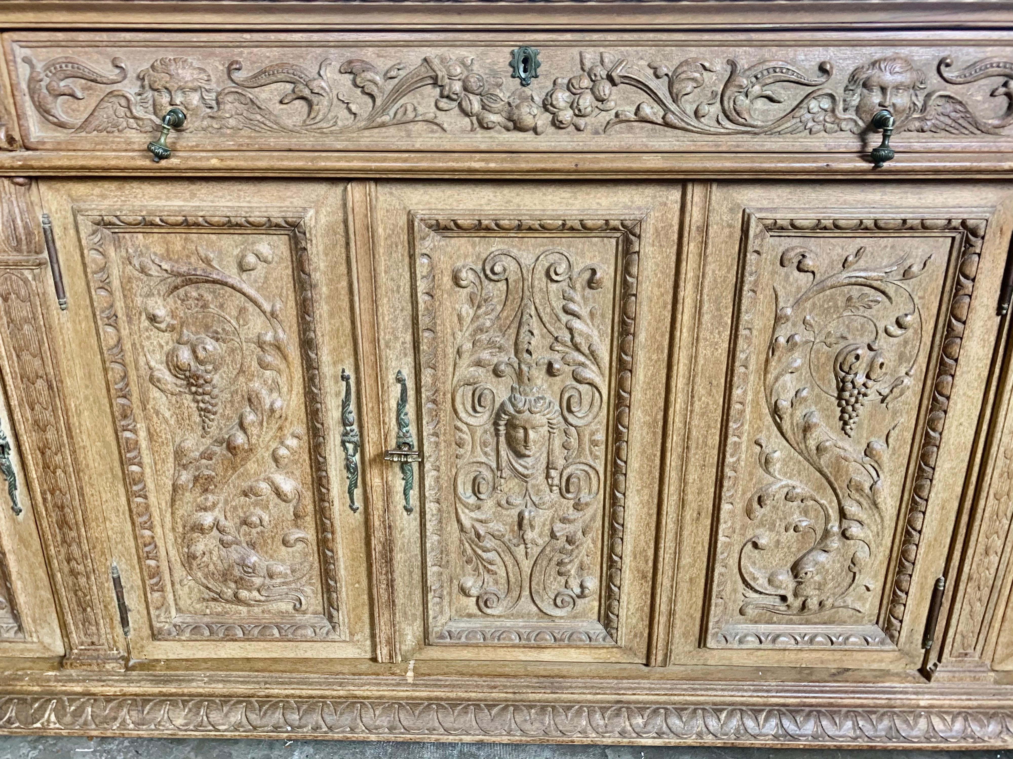 Italian bleached finely carved walnut credenza depicting grape vines, cherubs, scrolled acanthus leaves, faces and so much more. This piece has drawers and plenty of storage underneath. The credenza holds a black marble top with gold accents and