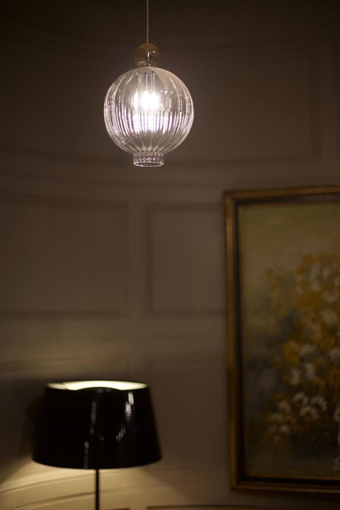 These are the glass Silhouette pendant lights made entirely by hand in Italy. The glass shade is clear with lined details and an amber coloured glass ball on top. They cast a beautiful even light in a space. Great as single pendant lights or used in