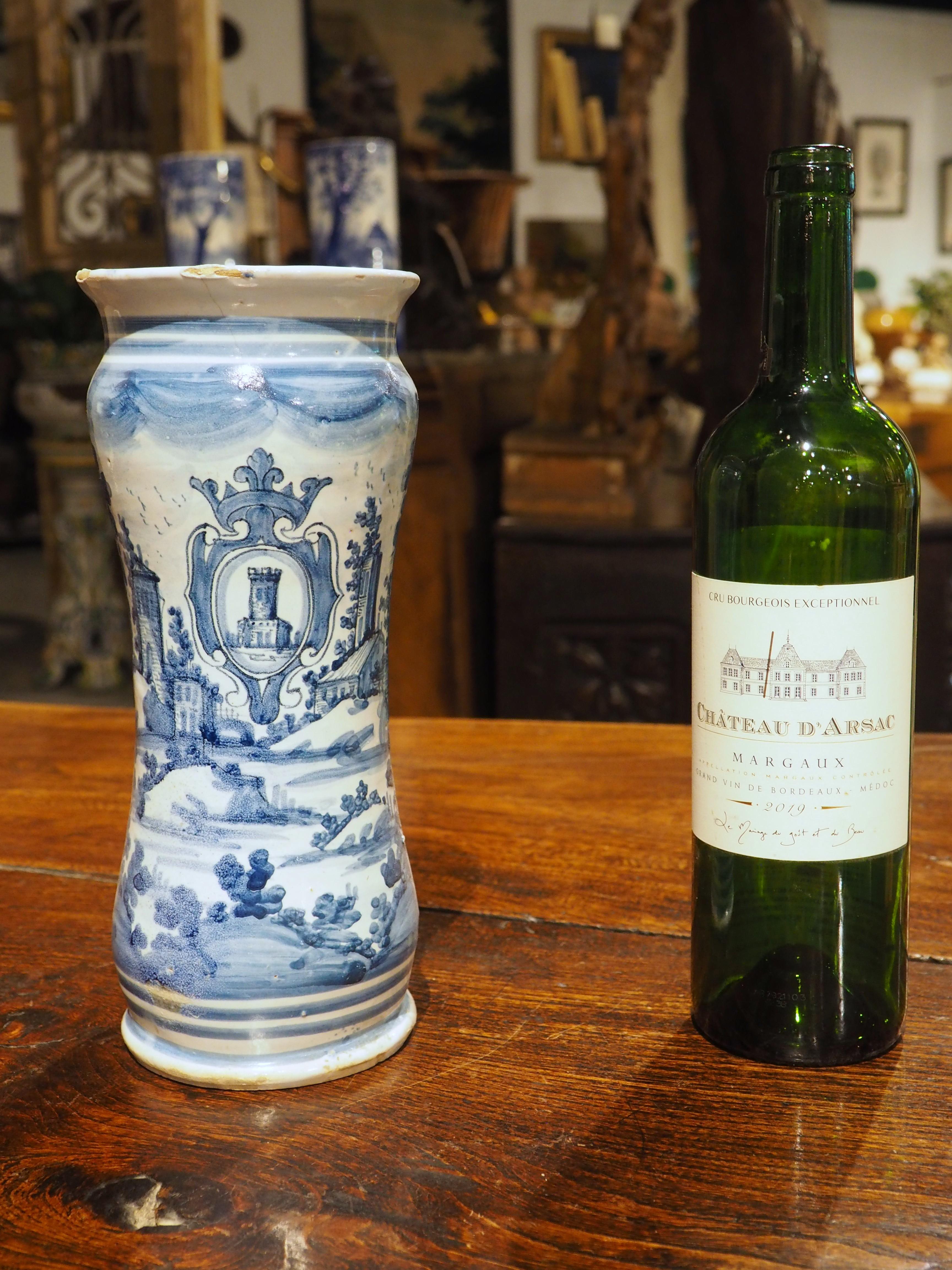 Dipinto a mano con un paesaggio pastorale sotto uno stemma, questo vaso Albarello italiano del 1800 presenta una bella tavolozza di blu cobalto e bianco. Il cartiglio araldico raffigura un castello circondato da un'elegante console sormontata da una