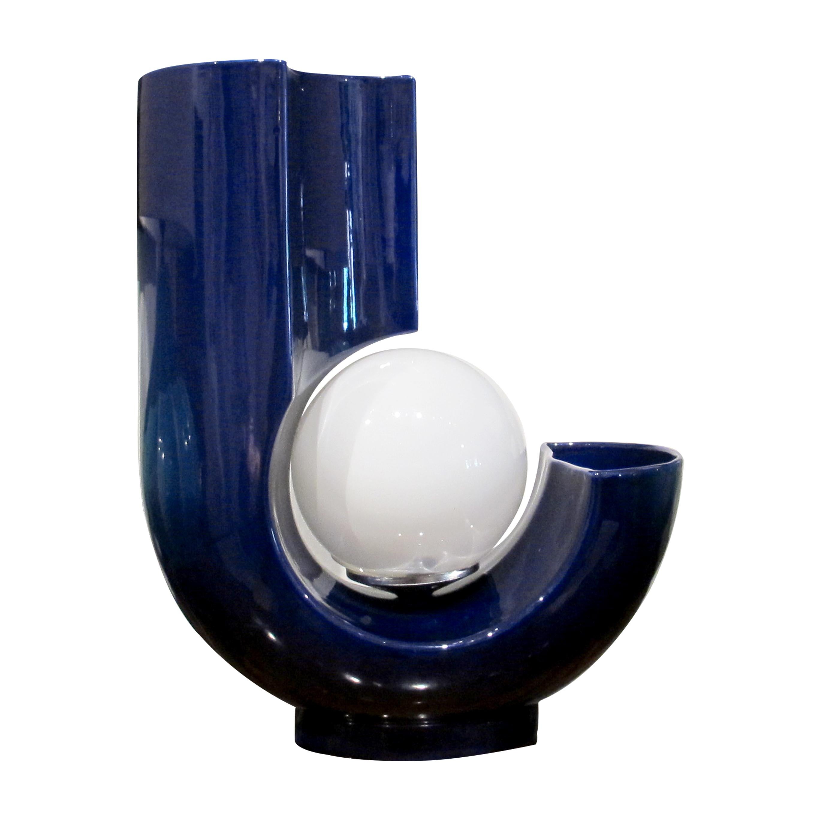 Cette lampe de table sculpturale, un design italien des années 1970, présente une forme en U audacieuse fabriquée en céramique bleu cobalt riche et brillante. Un globe en verre opale incandescent projette une lumière chaude et diffuse en son centre,
