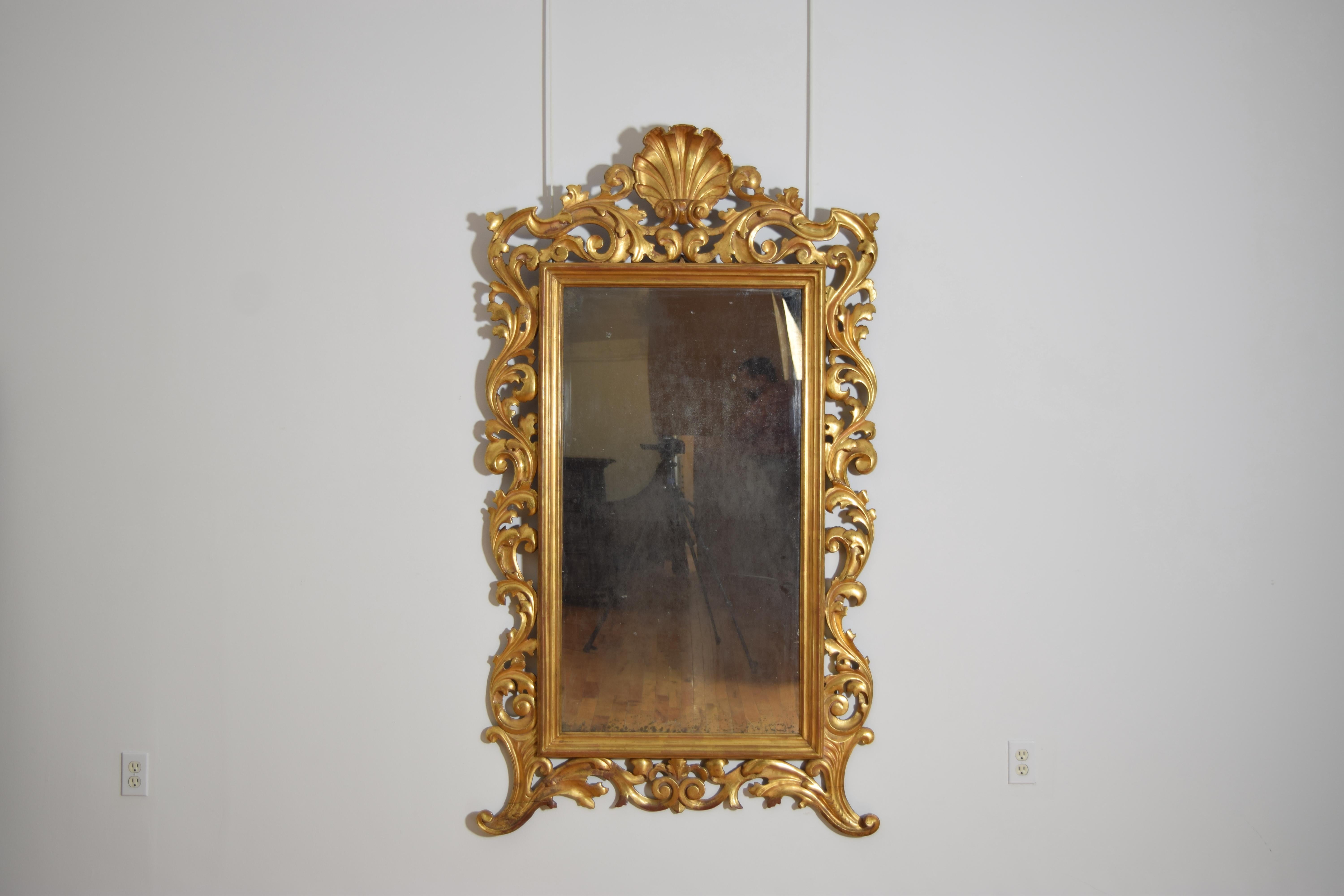conservant sa feuille d'or 23K brillante d'origine, avec une plaque de miroir antique rectangulaire centrale dans un cadre à bord mouluré, le cadre entouré de rinceaux en forme de feuilles, le dessus surmonté d'un grand coquillage sculpté, le bas