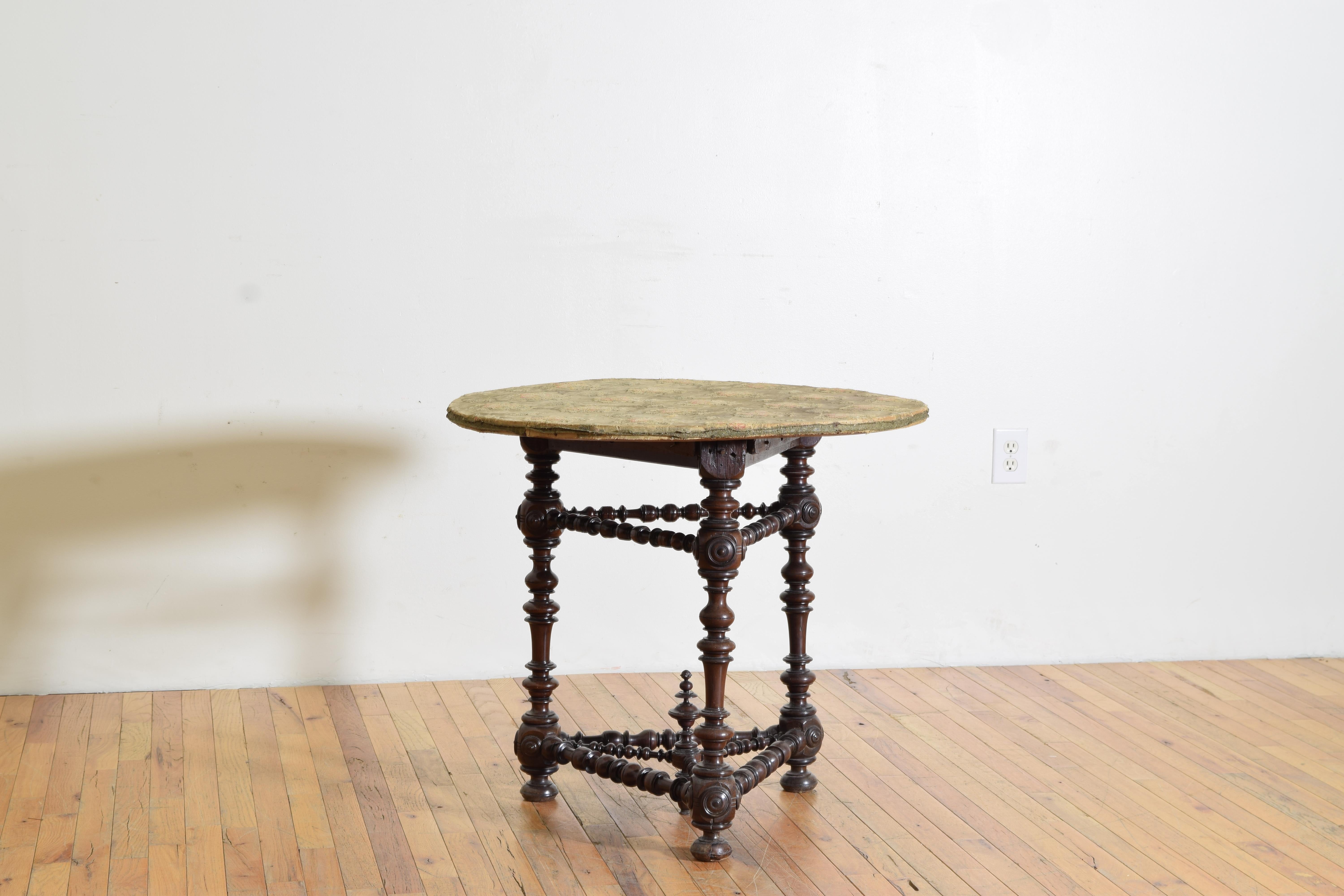 Having a circular, later, upholstered top resting on a three-leg frame of turned walnut, the stretchers also expertly turned, the corners with turned medallions