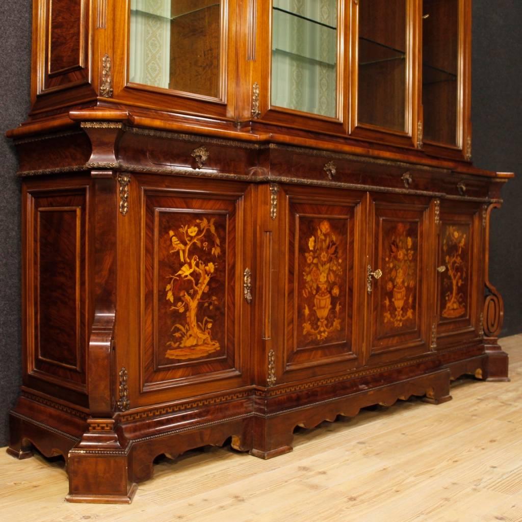 Italian bookcase from 20th century. Furniture in richly carved and inlaid wood with floral decorations in walnut, burl, rosewood, maple, tulipwood and fruitwood. Double body bookcase with four doors and four drawers in the lower part. Upper body
