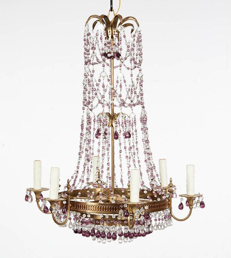 Un elegante lampadario a cestello italiano sormontato da fronde arcuate in ottone da cui si dipartono eleganti volute colorate di ametista e trasparenti fino a un anello di ottone forato che sostiene sei candelabri in metallo dorato con bracci e