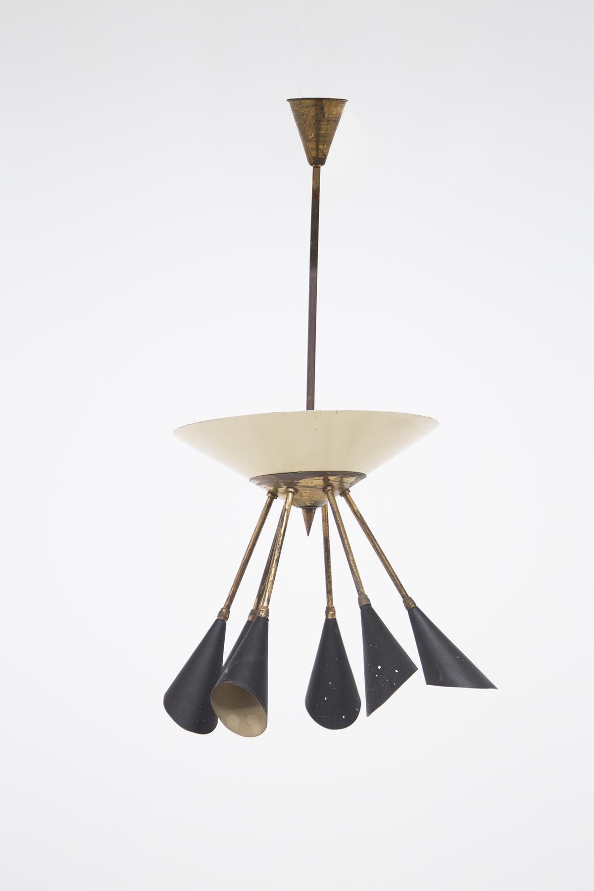 Vintage Italian-made chandelier from the 1950s. The chandelier is made with a patina brass frame. At the end of the brass stem we find an inverted pyramidal dome in white painted aluminum, its tip is finished in brass. From it we radiate six brass