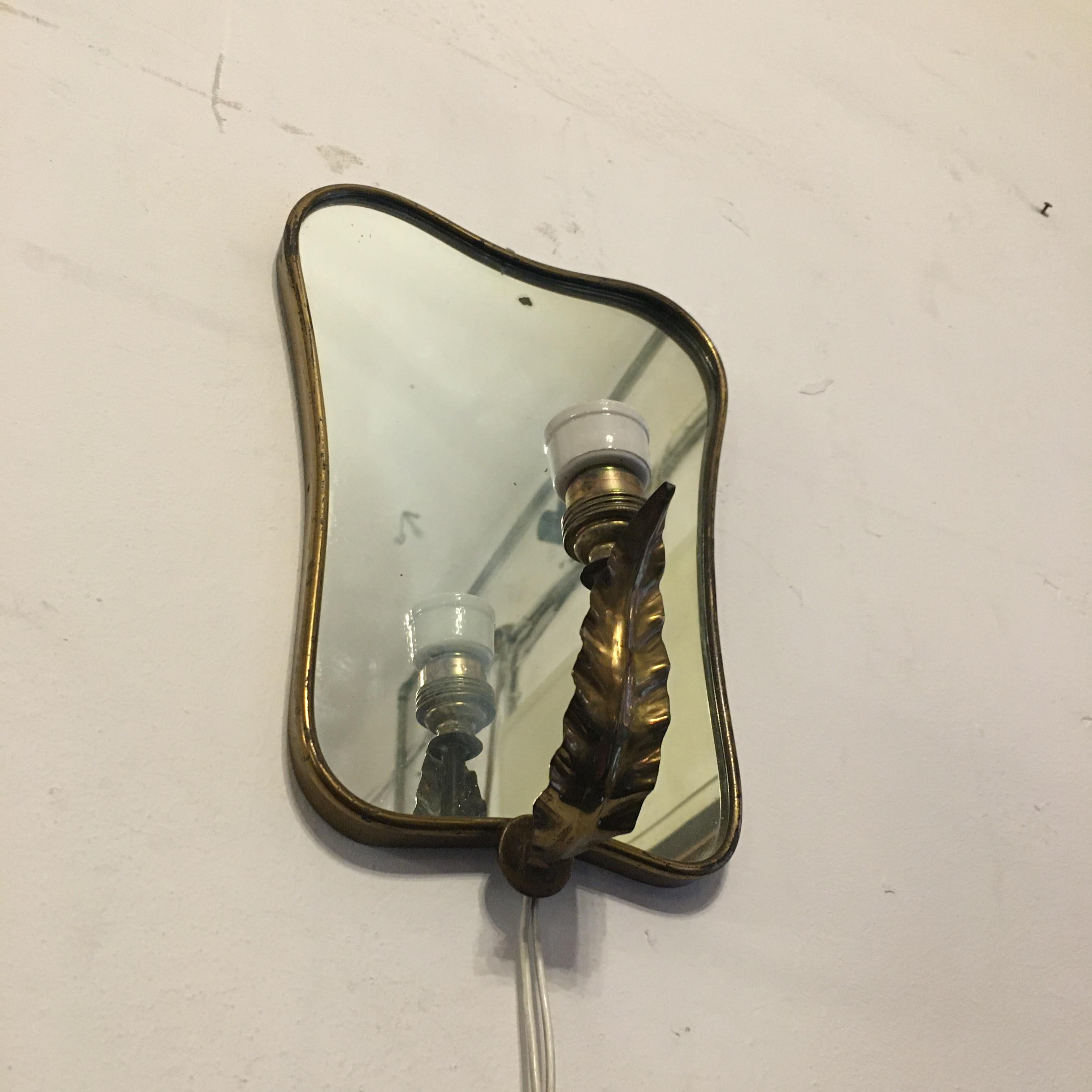 Italian brass and ceramic wall mirror, 1950s. Small wall mirror equipped with its original ceramic lamp holder; golden frame and brass decoration, 1950s.