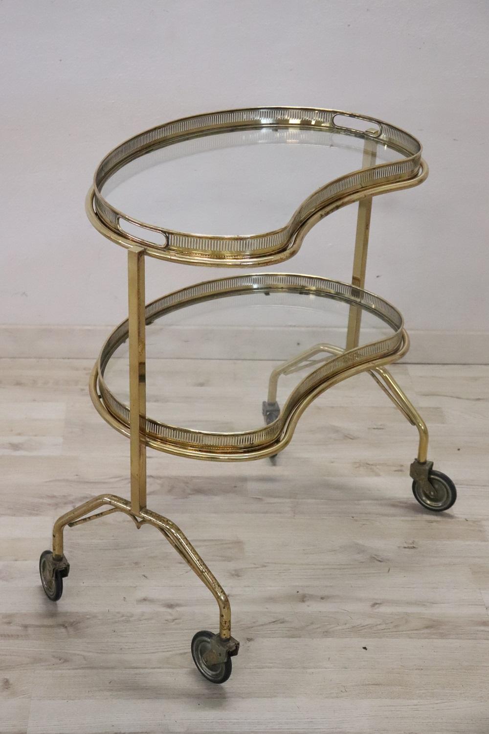 Rare bar cart Italian 1980s, it is made of golden brass and glass. The brass is finely worked. Comfortable wheels they allow easy movement. Equipped with two glass top, the upper top is equipped with handles and can be used as a tray to serve
