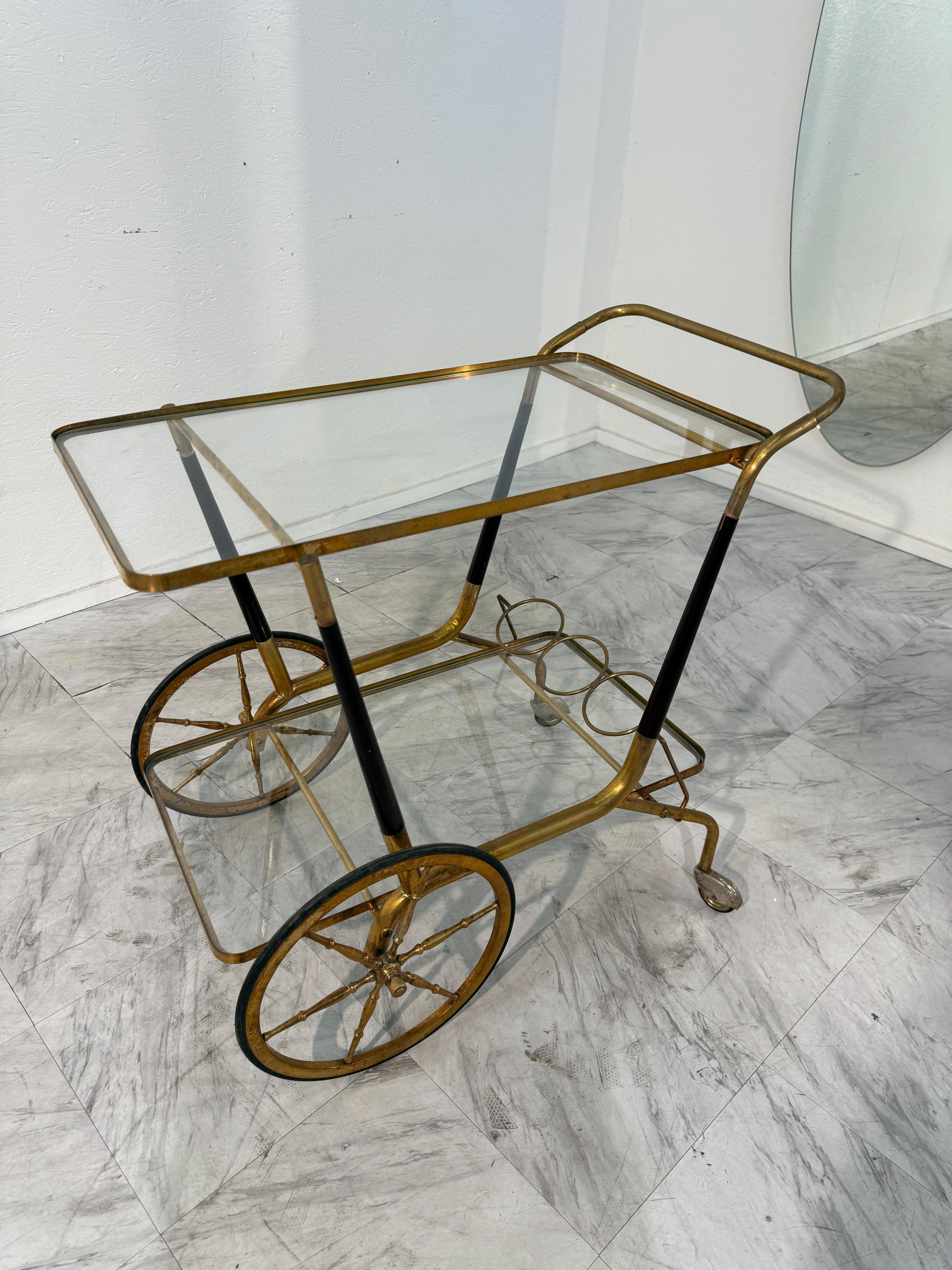 Este elegante carrito de bar italiano de mediados de siglo, de la década de 1950, combina un diseño refinado con la funcionalidad. Fabricada con un marco de latón pulido, presenta dos niveles de superficies de cristal transparente que proporcionan