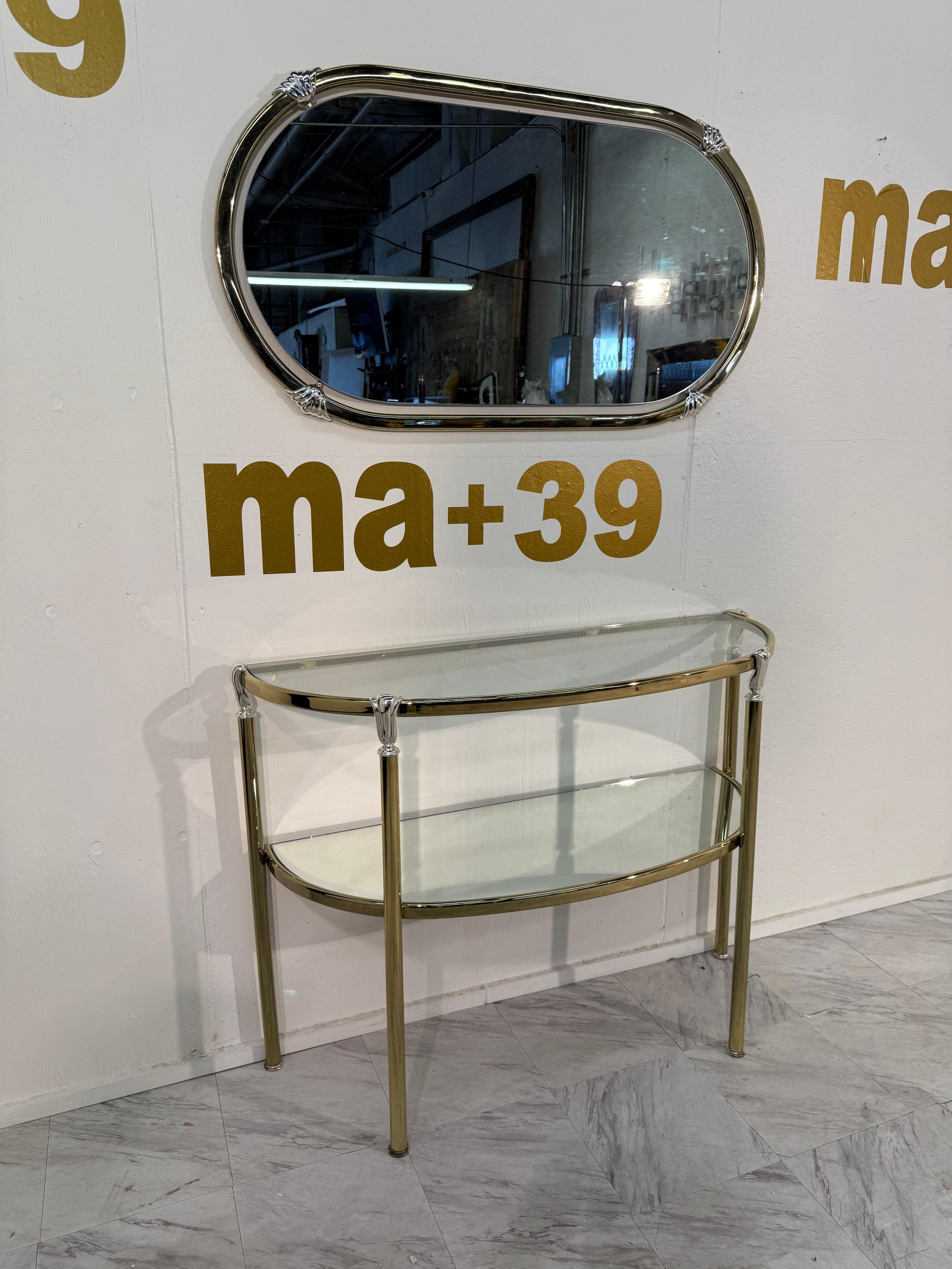 Elegante conjunto italiano de consola y espejo de los años 70, que encarna el refinado glamour de la época. La consola demi-lune presenta un marco de latón pulido con dos niveles de estantes de cristal transparente, que ofrecen funcionalidad y