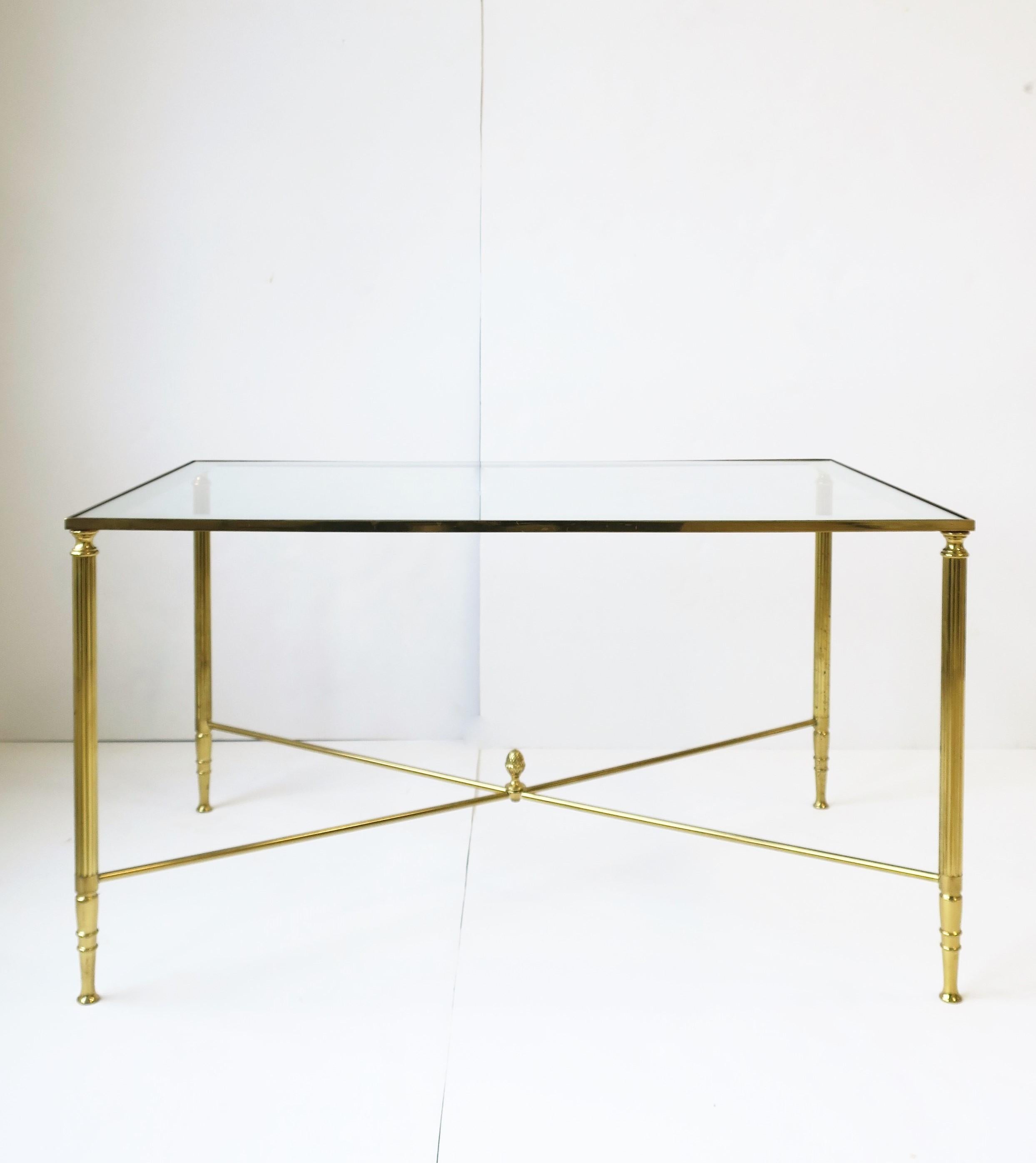 An elegant rectangular brass and glass coffee/cocktail table with stretcher base and finial top, in the Directoire design style, circa mid-20th century, 1960s. Glass top with mirror edge detail around is inset into table base frame. In the Masion