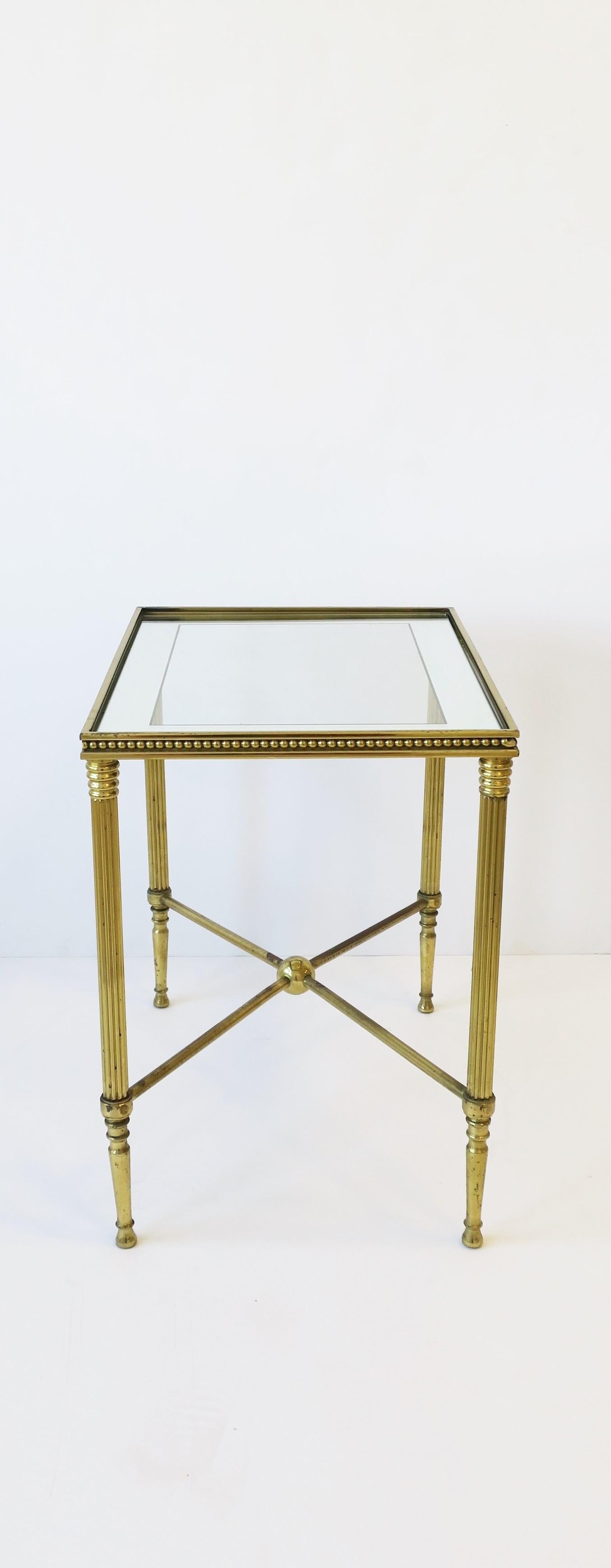 A beautiful mid-20th century Italian brass and glass rectangular end or side table in the Directoire style after maker Maison Jansen, circa 1960s, Italy. Glass top with mirrored edge is 'inset' into brass frame which has beautiful bead detailing
