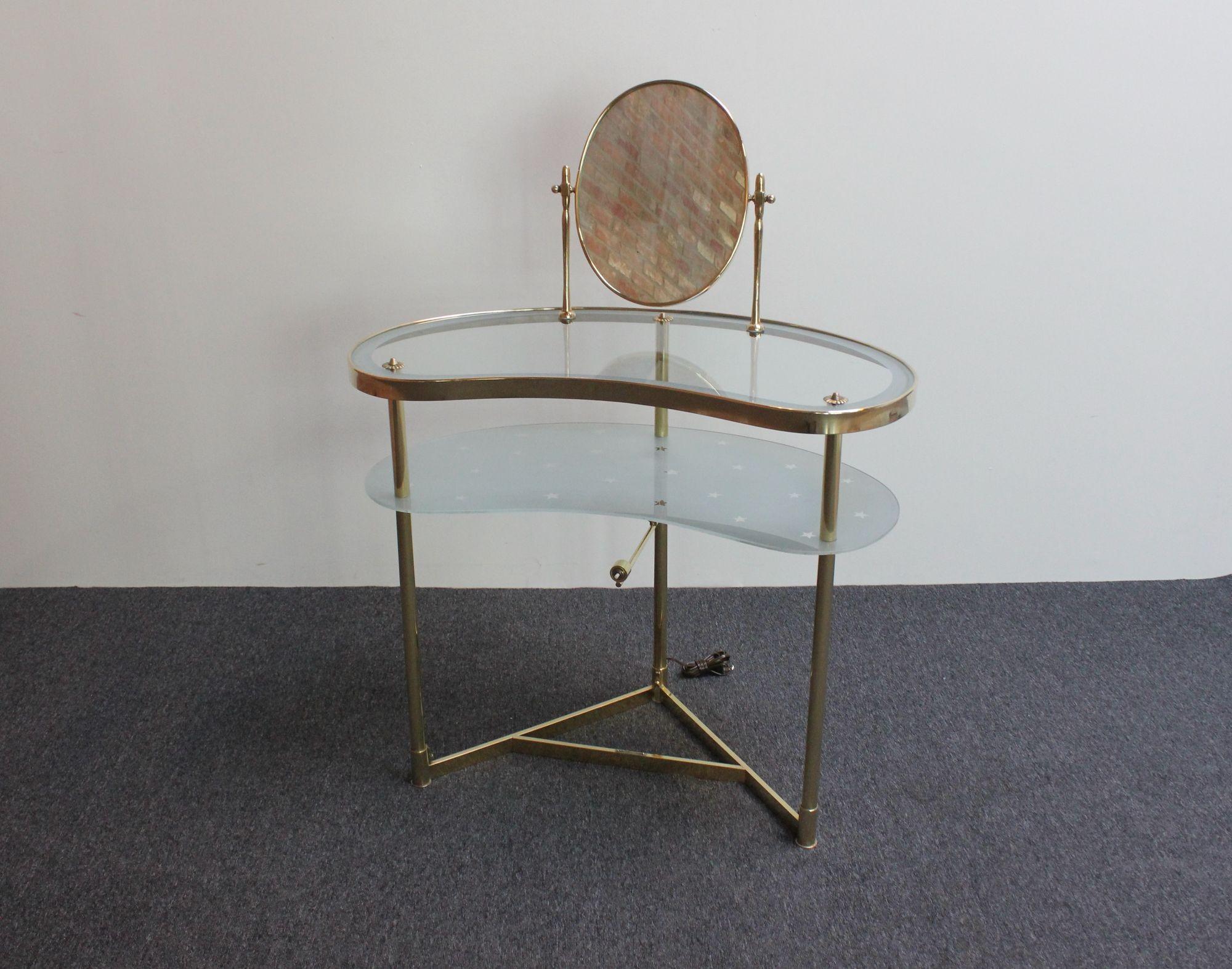 Élégante coiffeuse/lavabo avec éclairage, conçue par Luigi Brusotti (vers les années 1950, Italie).
Composé d'un miroir pivotant en laiton monté sur une table de toilette avec un plateau supérieur en verre transparent et un plateau inférieur en