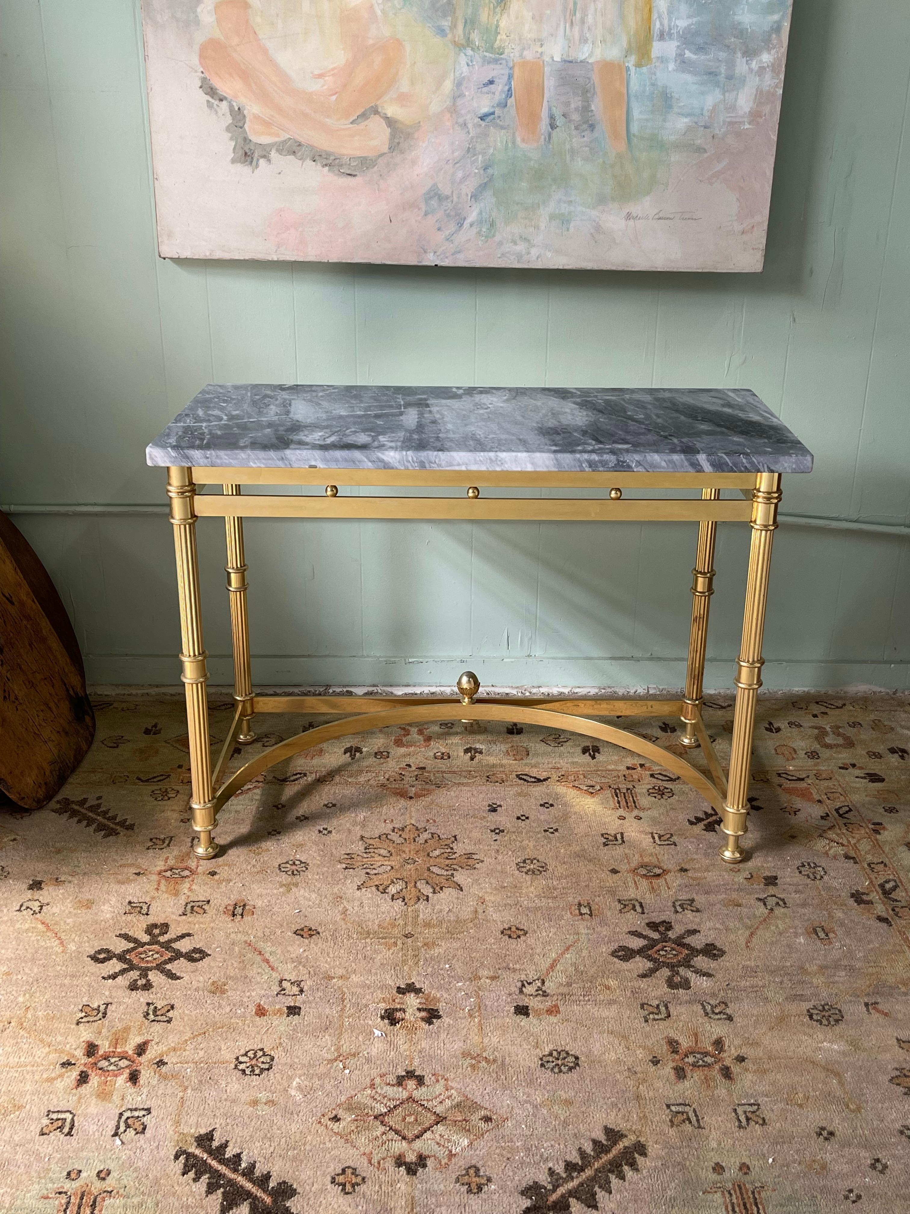 Fine quality mid 20th Century Italian neoclassical style console table having a gray marble rectangular top over a polished brass base with fluted legs and beautifully curved stretchers.